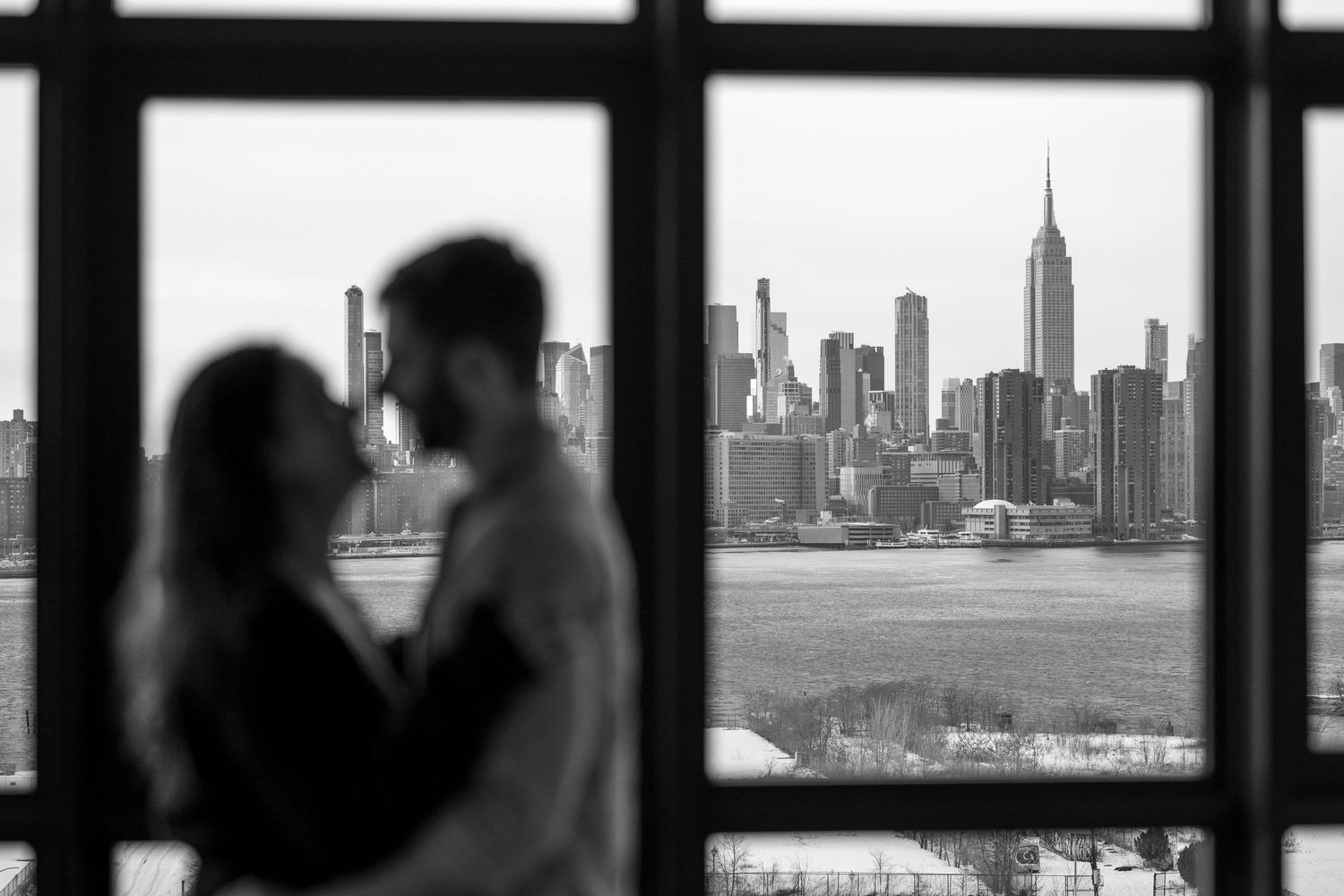 A black and white cityscape view of Chicago's skyline seen through large windows with silhouetted figures in the foreground.