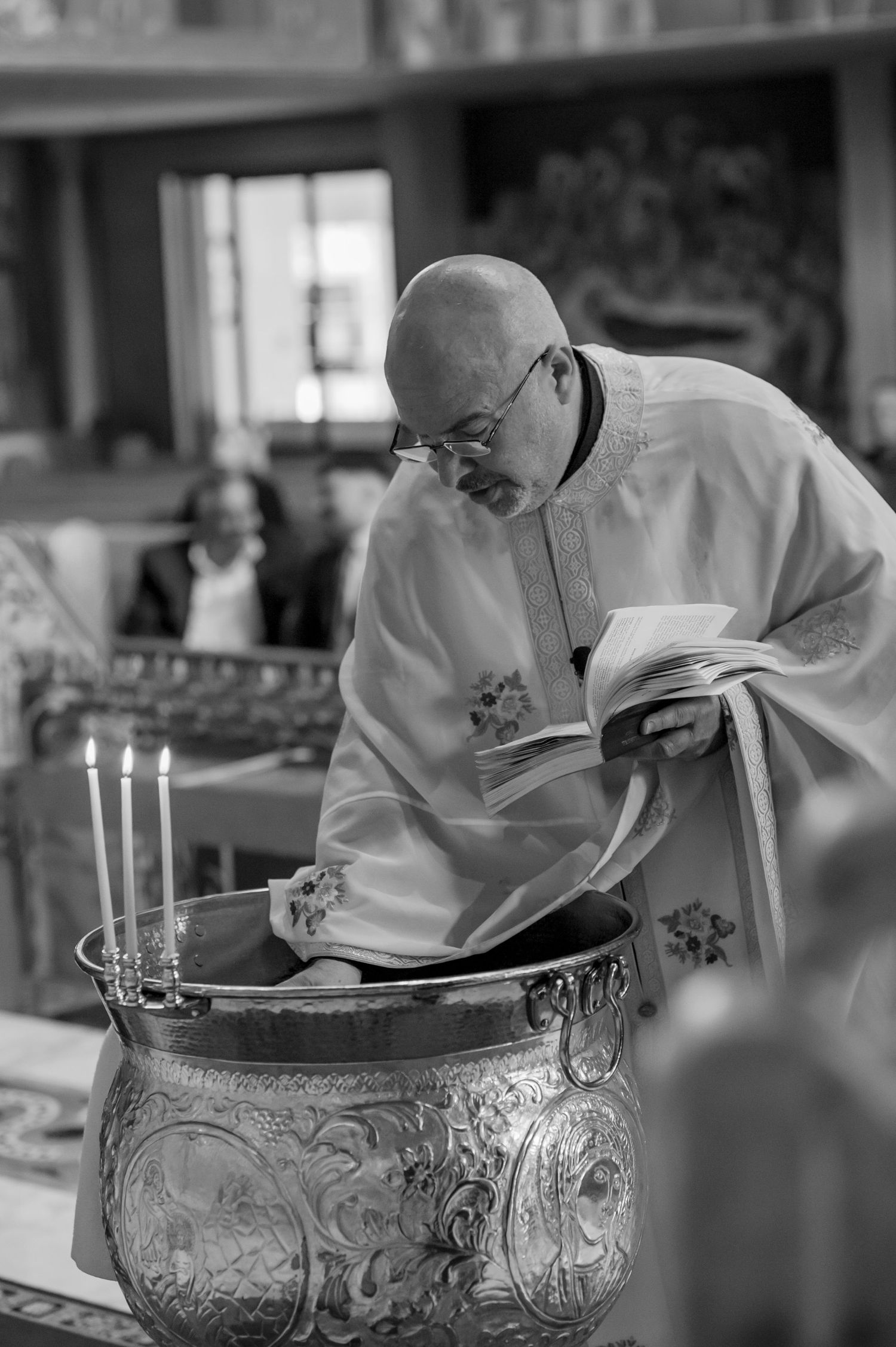 A close-up shot of a decorative silver baptismal font with ornate engravings and lit candles.