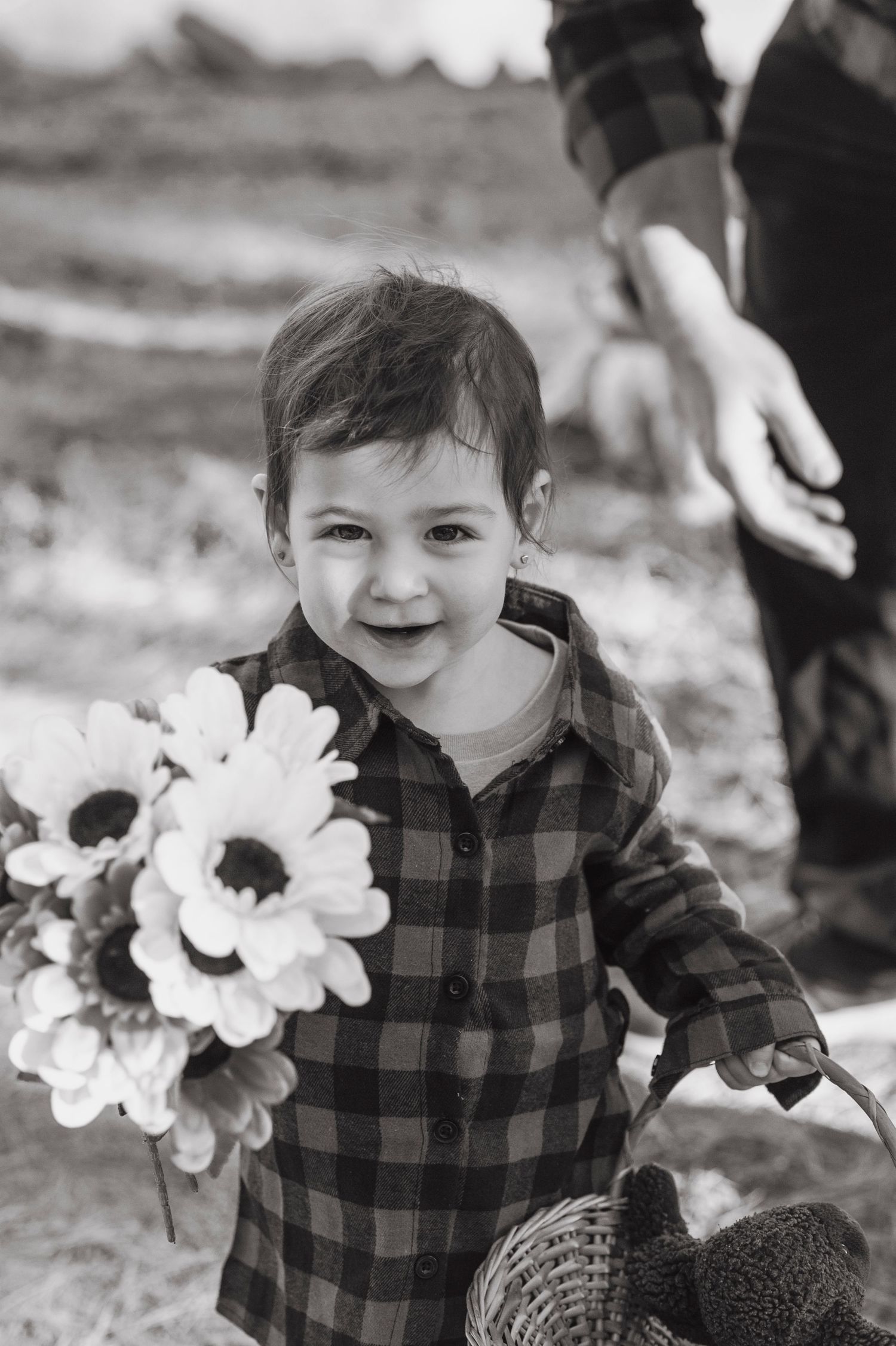 Child in buffalo plaid shirt poses with white flowers in black and white photography series.