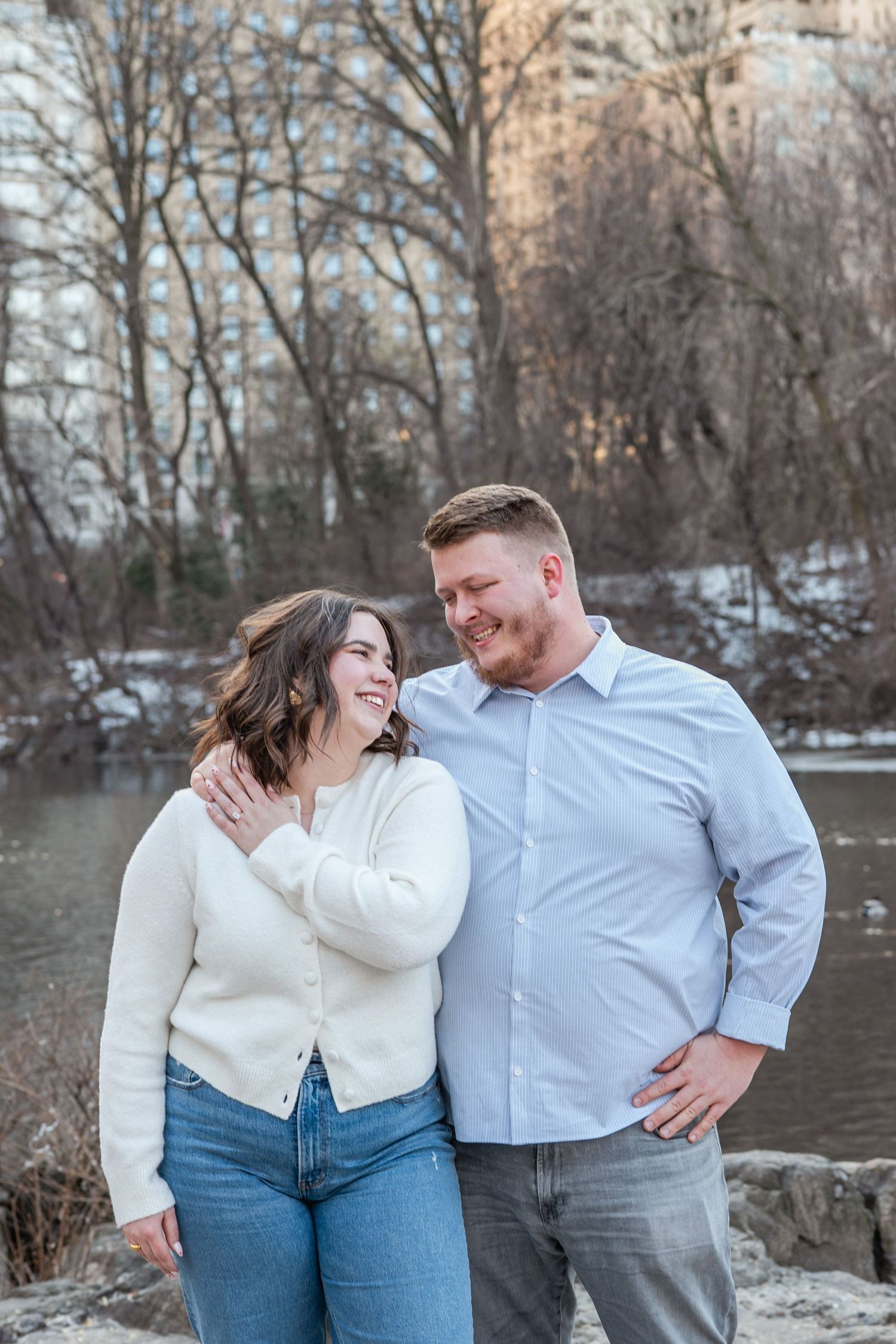 A couple shares joyful moments together by a snowy lake during a winter engagement photo session.