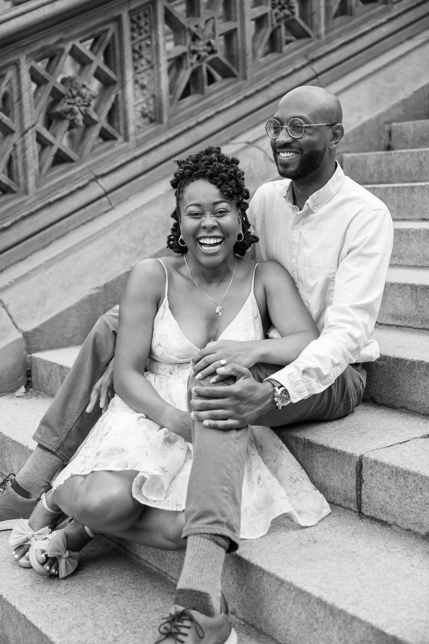 A joyful couple sitting and laughing together on stone steps in a black and white photo series.