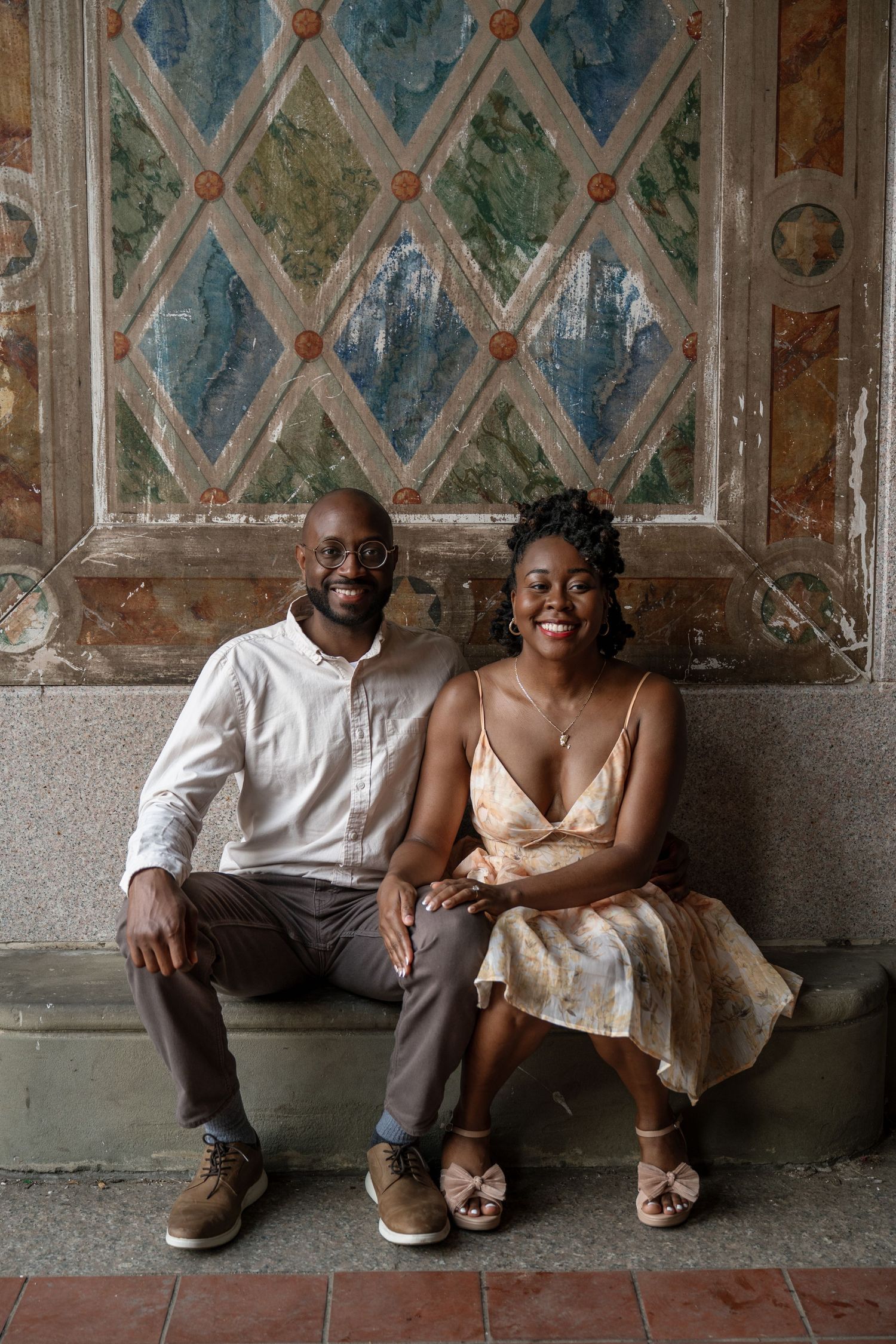 A couple relaxes against a decorative wall with painted diamond patterns.