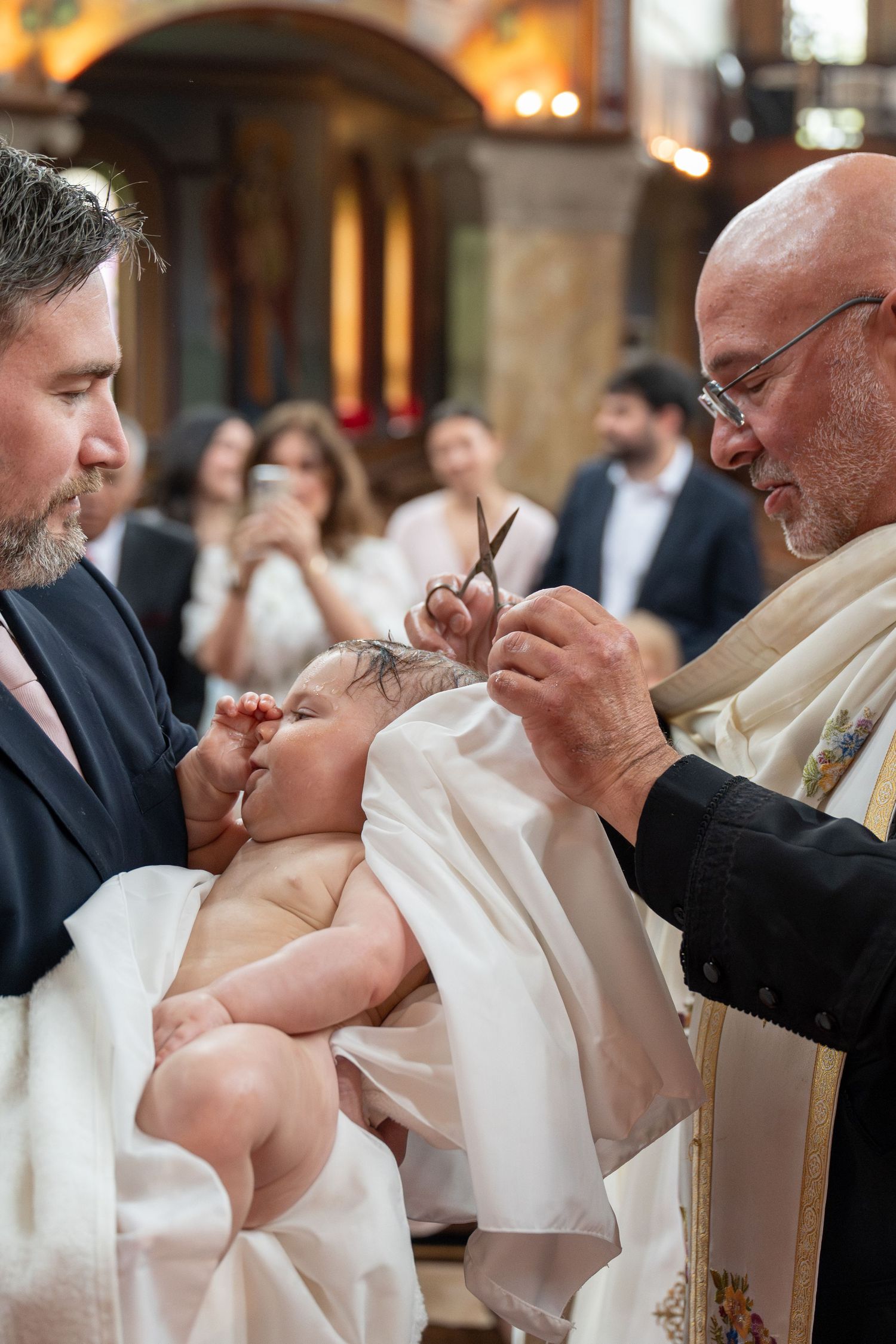 Priest cutting baby's hair during an Orthodox Christian baptism christening ceremony.