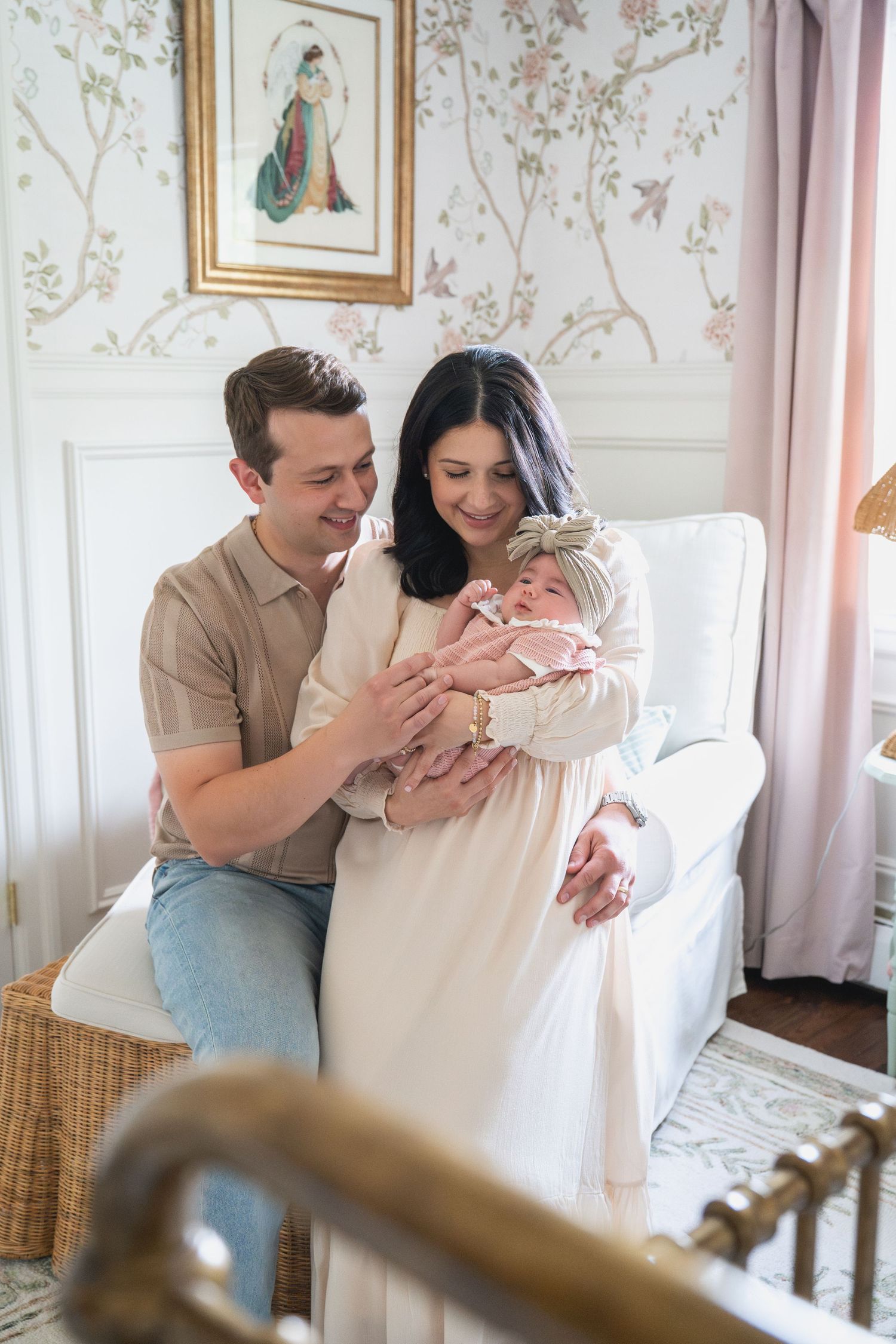 Family shares tender moments with newborn in nursery with floral wallpaper.