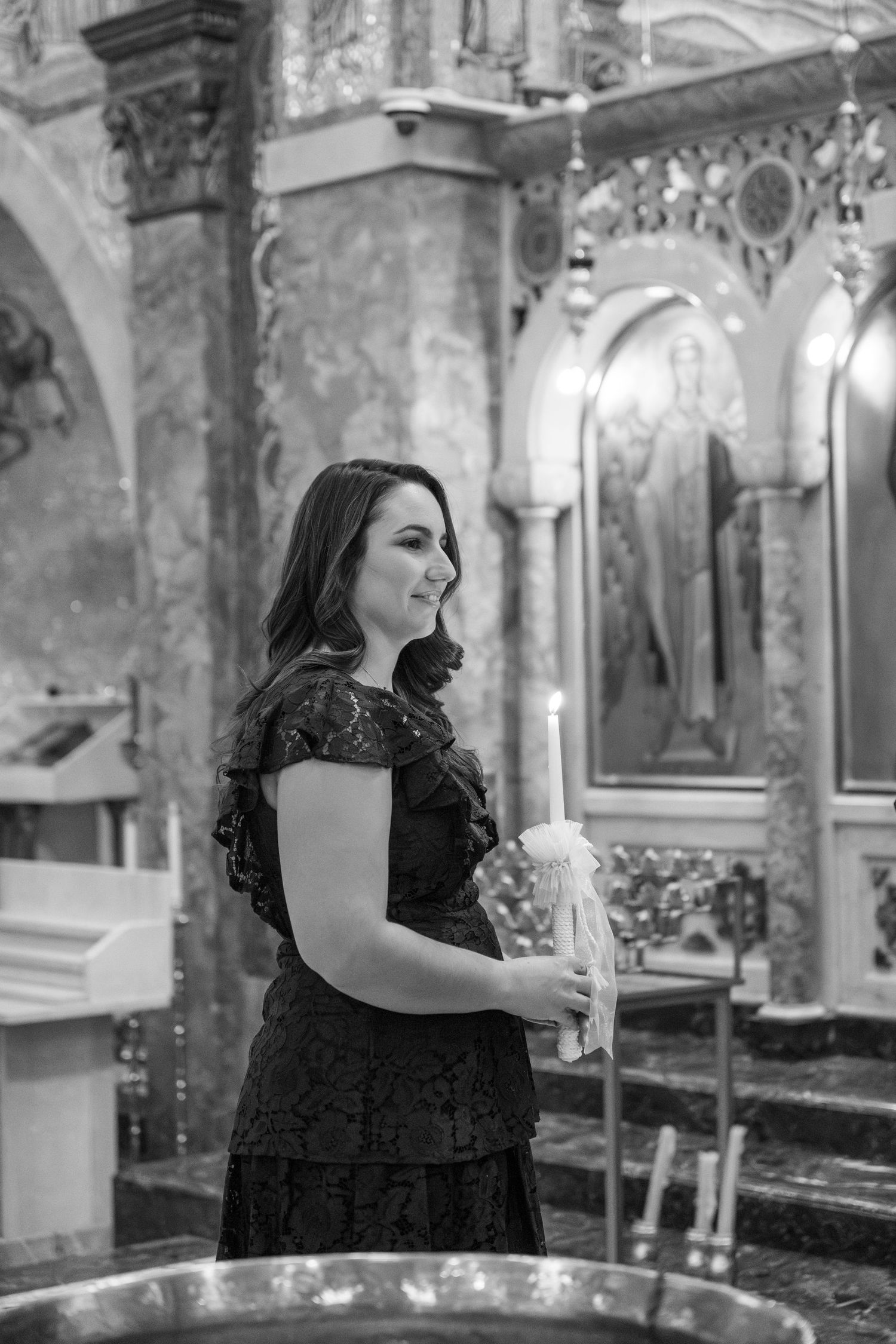 A woman in a black dress stands near religious candles inside a church with decorated walls and pillars.
