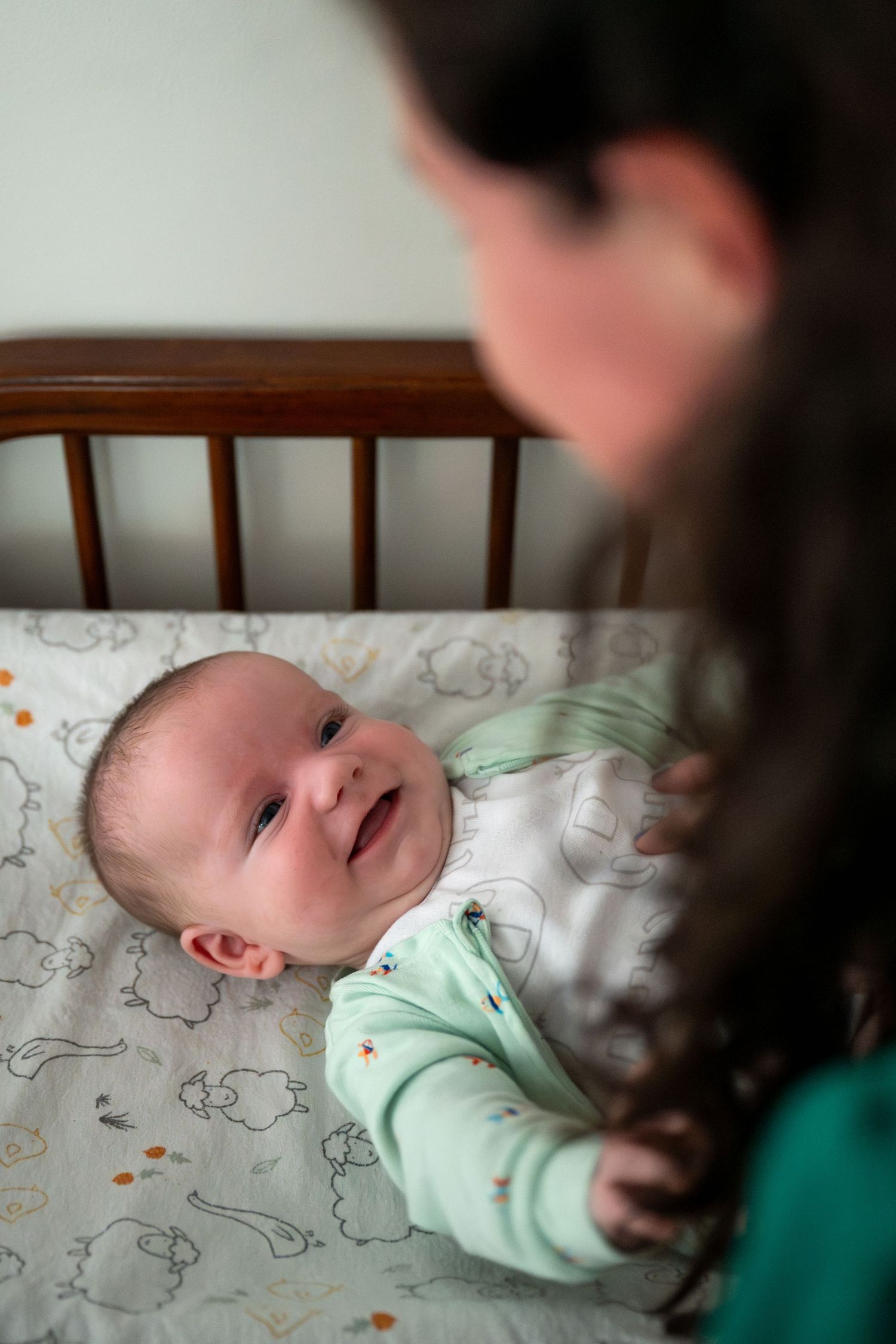 A baby wearing a mint green onesie lies on patterned bedding while being photographed from above.