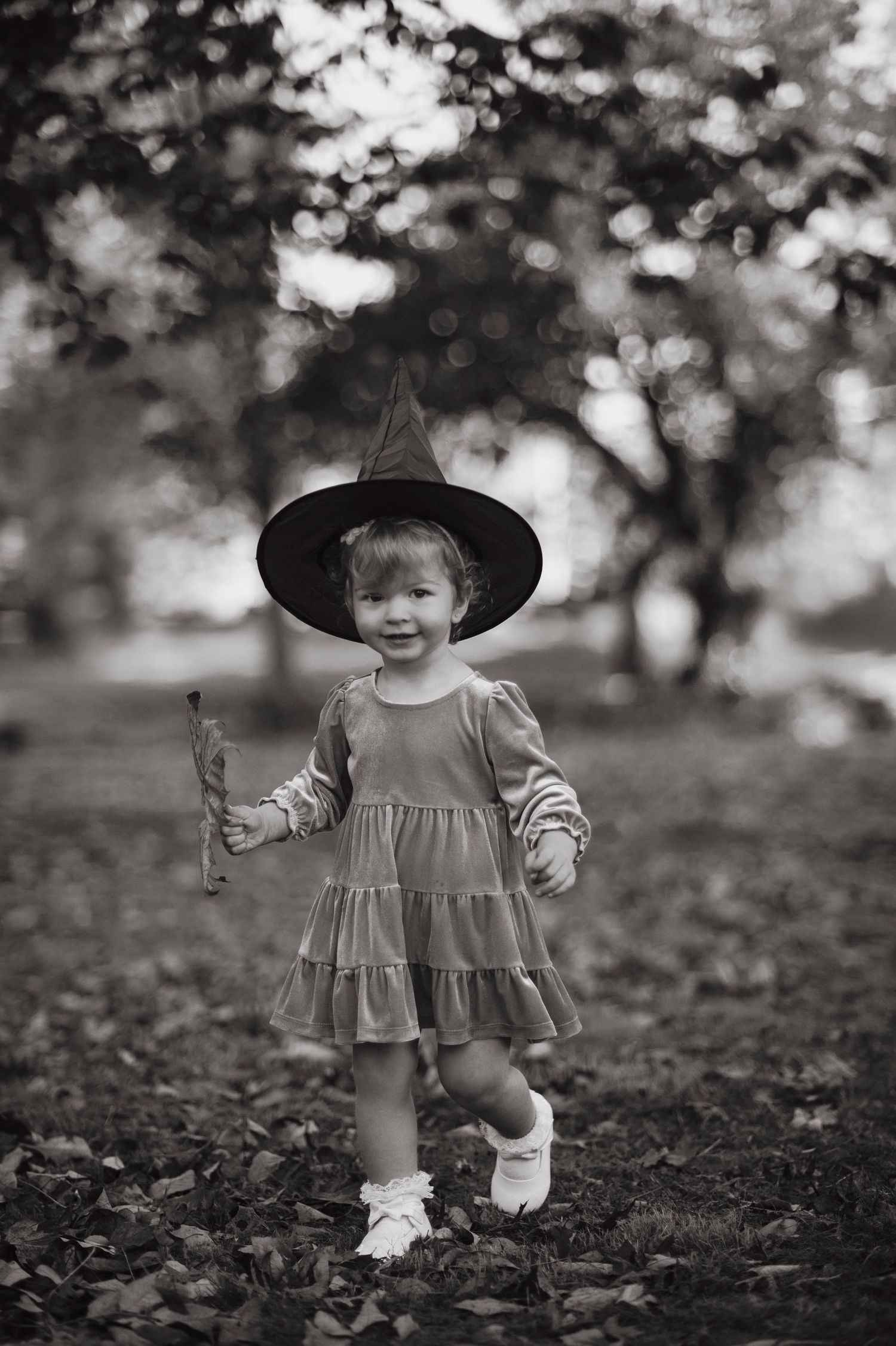 A series of black and white photos showing a toddler in a dress and hat playing outdoors.