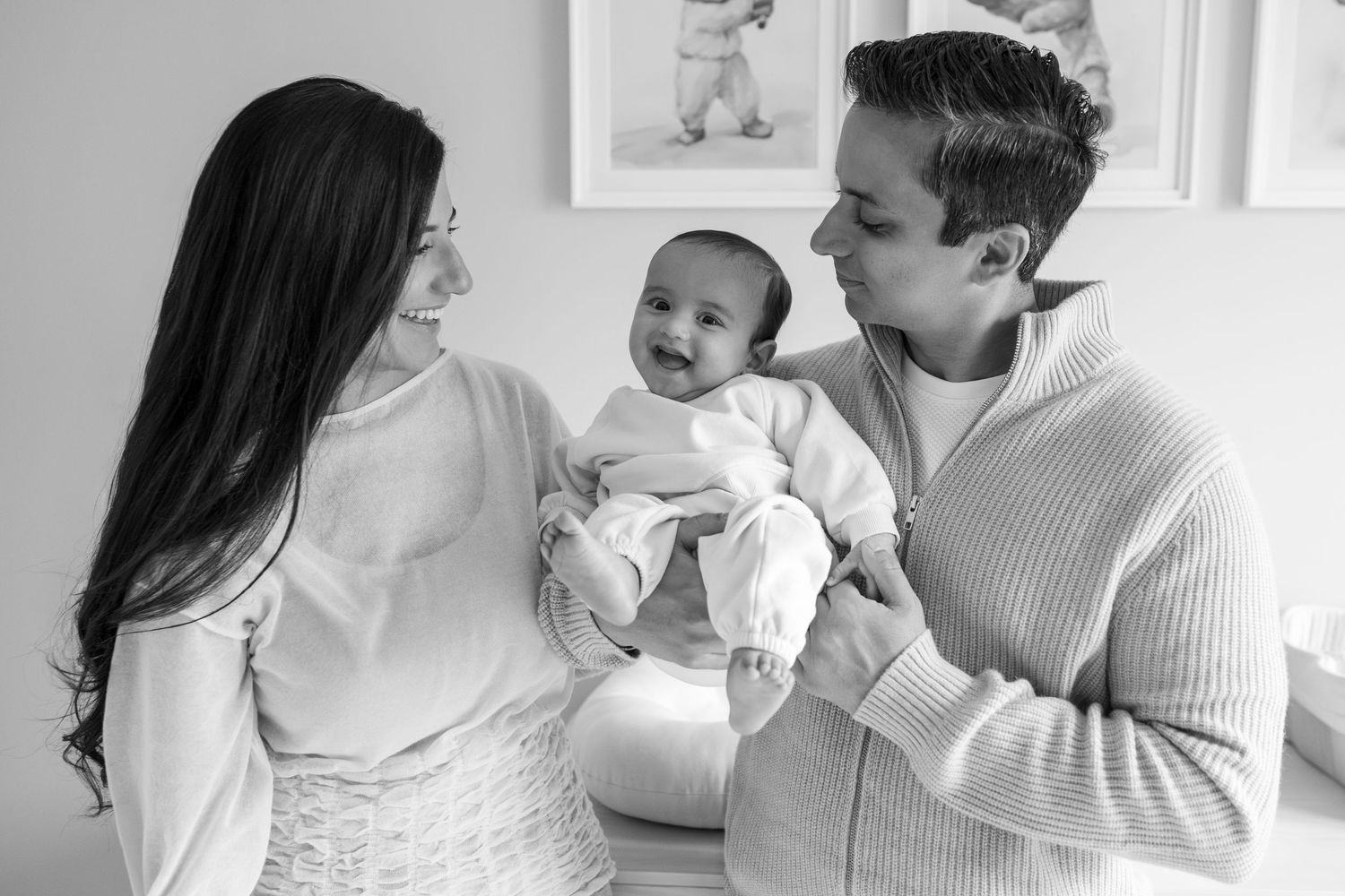 Black and white photo of a happy young family with mother, father, and smiling baby in a bright nursery room.