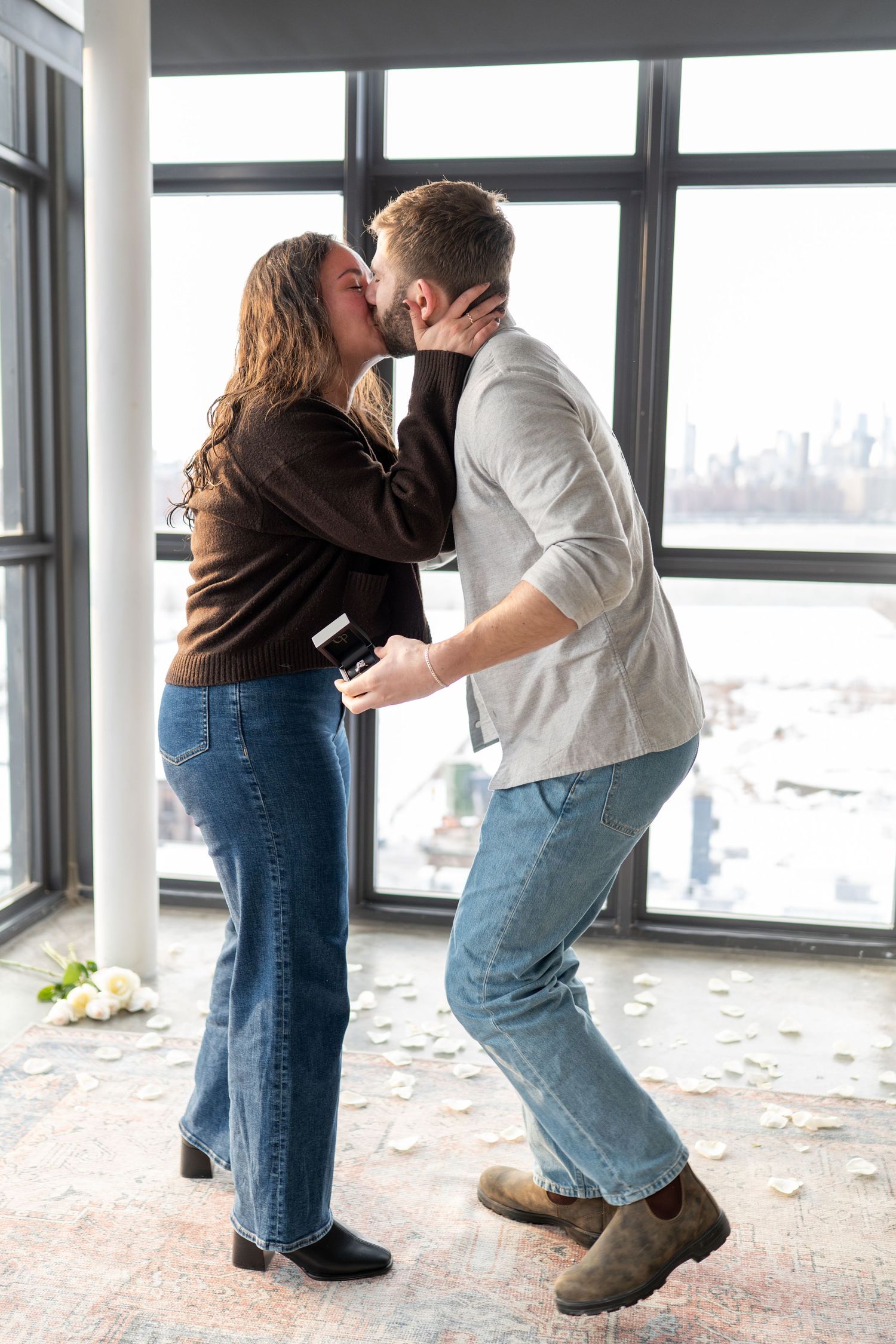 A couple in casual attire sharing a playful moment by a bright window in an urban setting.