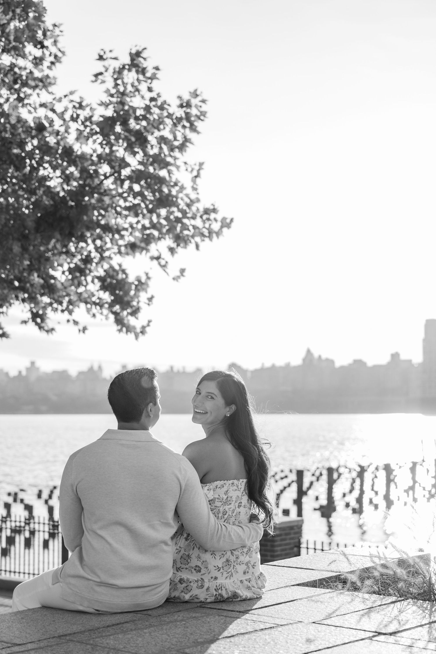 Black and white photo of couple relaxing on waterfront ledge at sunset.