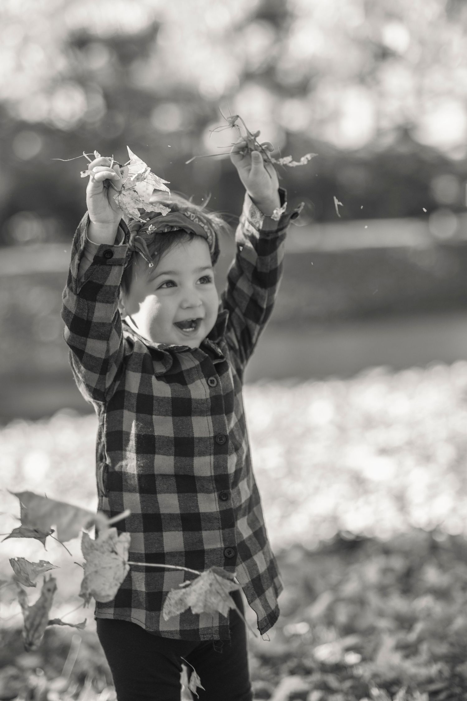 Black and white photo of joyful play with fallen leaves on an autumn day.