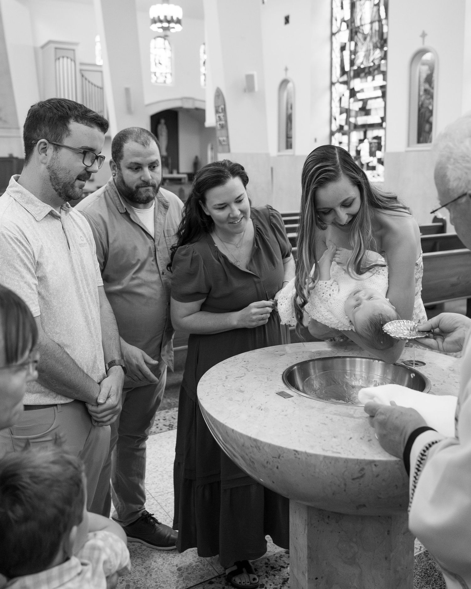 A group of people gathered around a large stone baptismal font in a church during a religious ceremony.