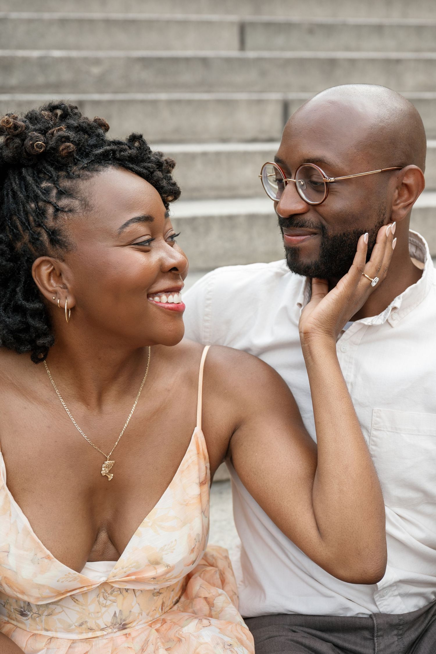 A loving couple shares a tender moment sitting on stone steps, with her in a floral dress and him in a white shirt.