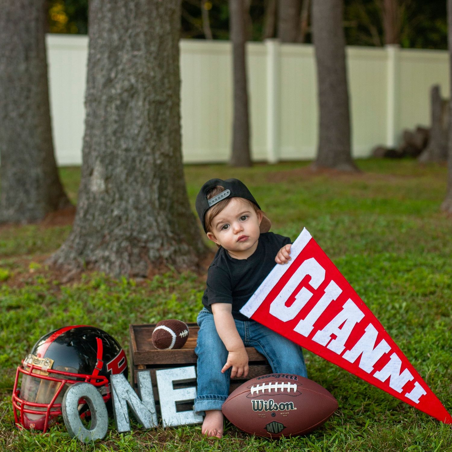 Football and decorative banners arranged around tree trunks for first birthday photoshoot.