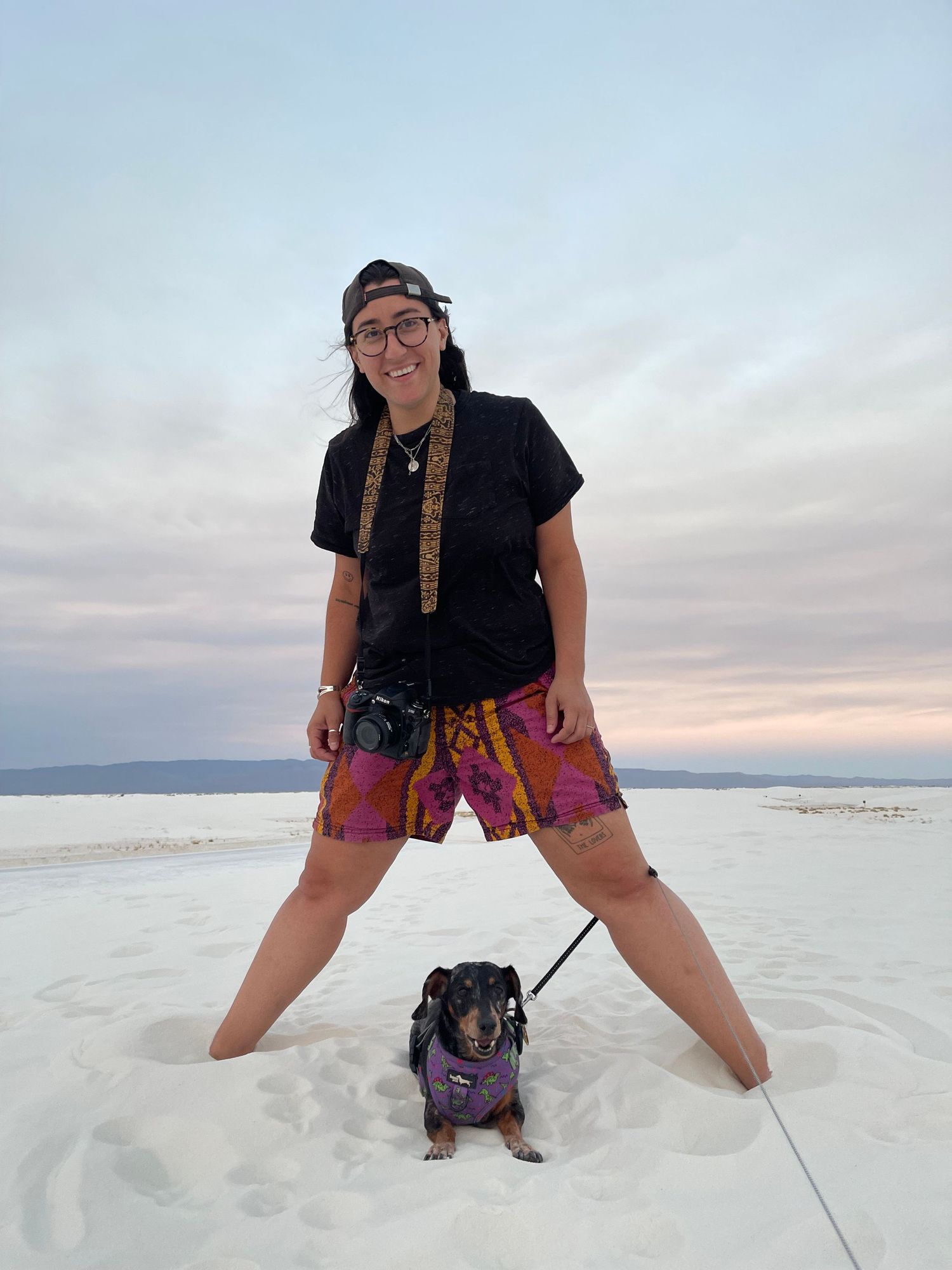 Person in patterned shorts poses on white sand during sunset.