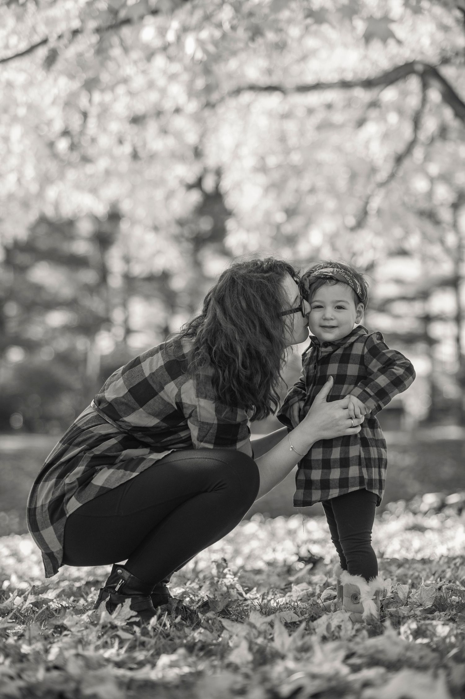 A tender autumn moment captured in black and white with matching plaid shirts under falling leaves.
