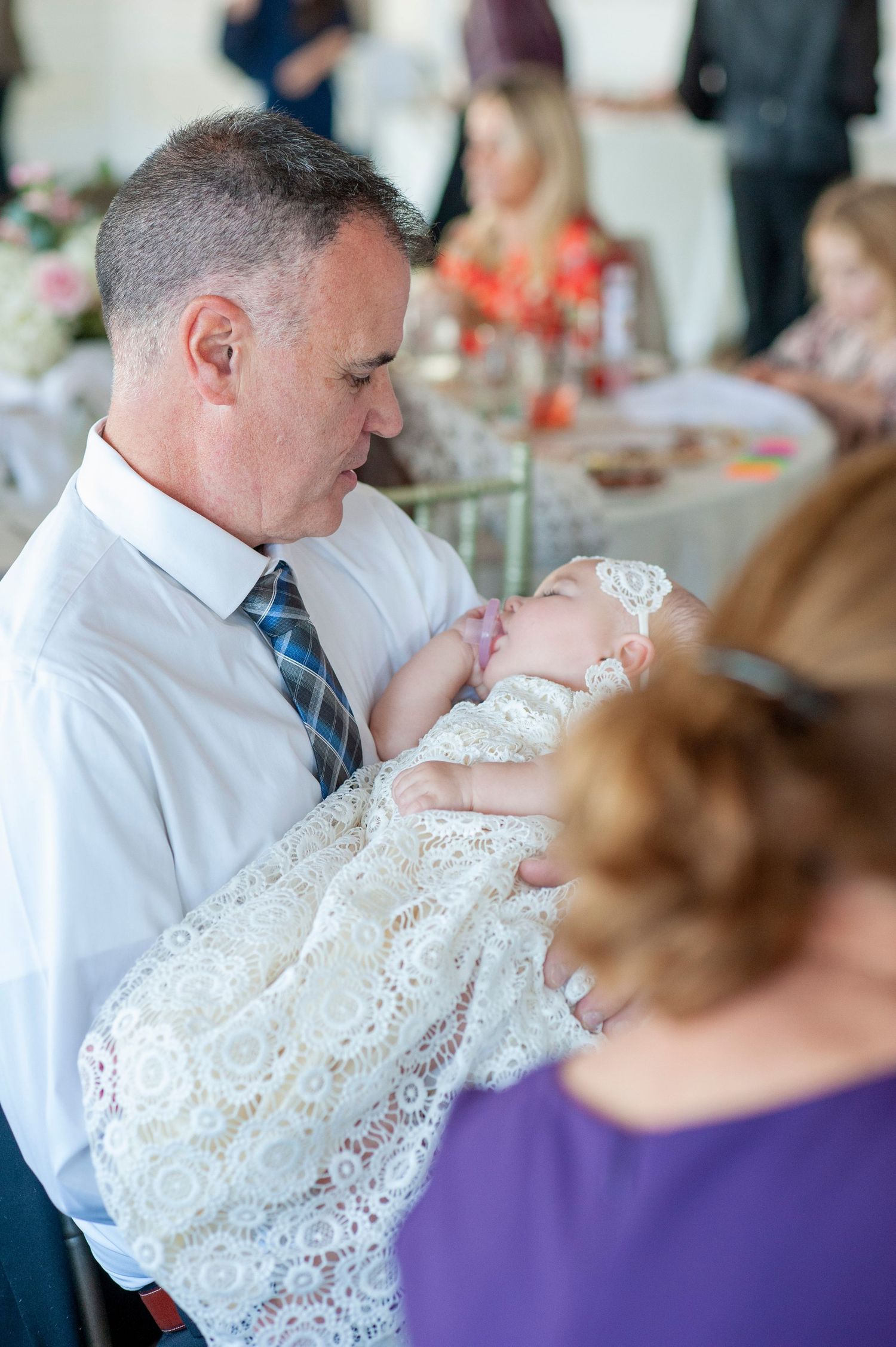 A baby in an ornate white lace christening gown is being held during a special ceremony.