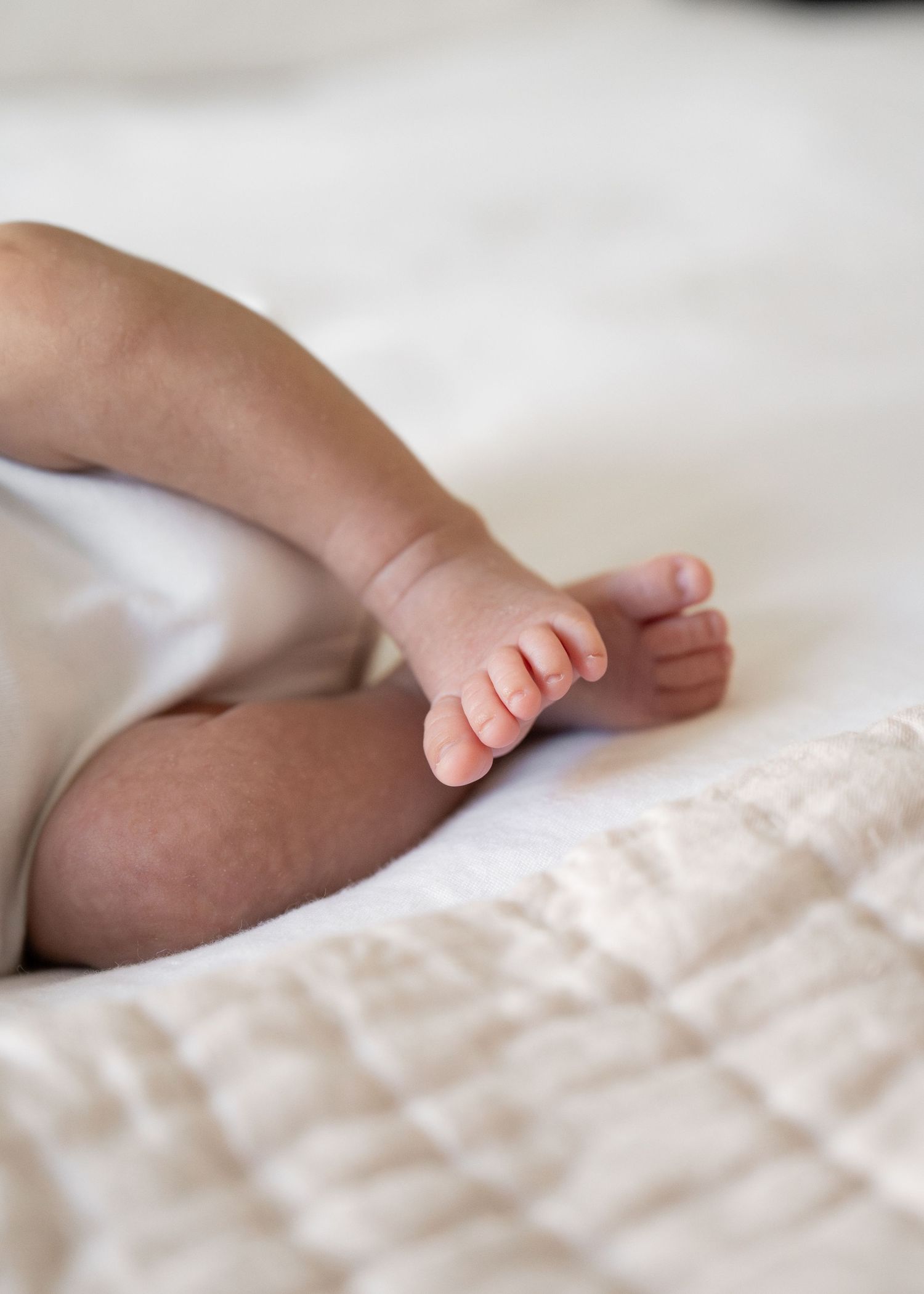 Close up of tiny baby feet resting on white textured bedding.