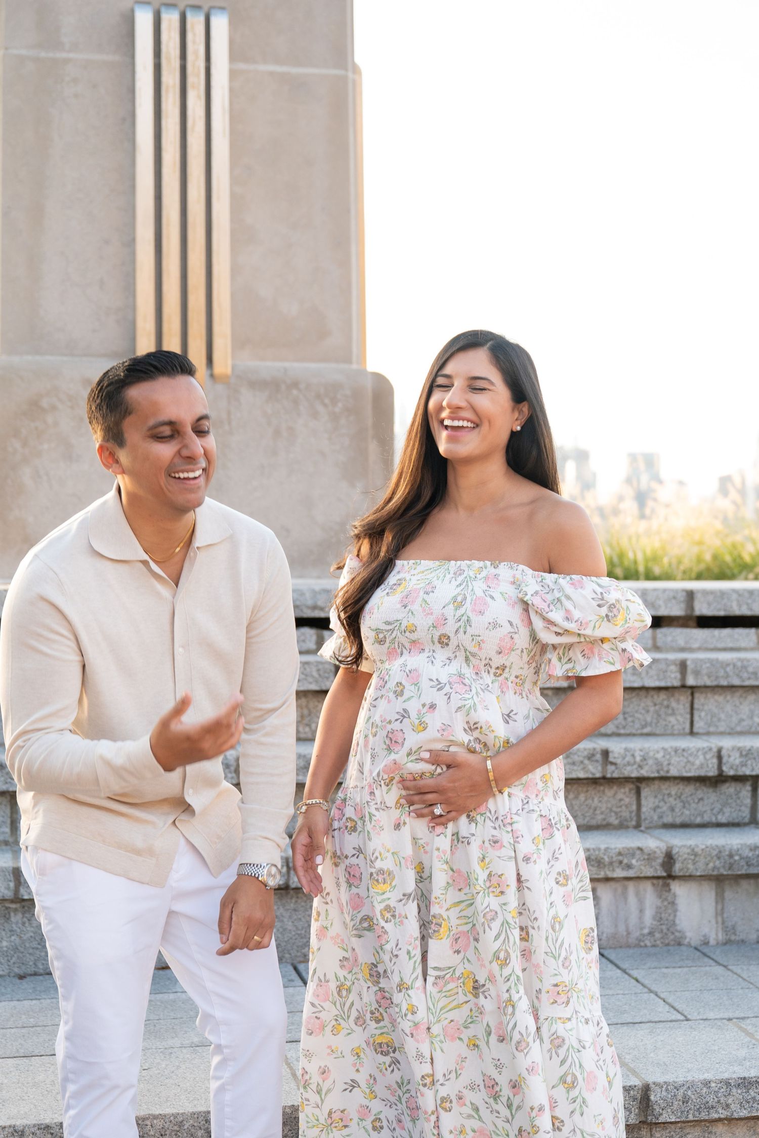 A couple shares joyful candid moments together on stone steps wearing coordinated white and floral outfits.