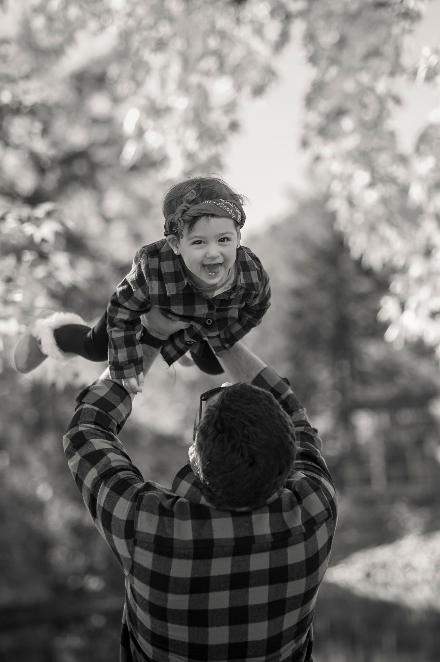 Black and white photo series showing joyful interaction between adult and child in buffalo plaid against blurred outdoor background.