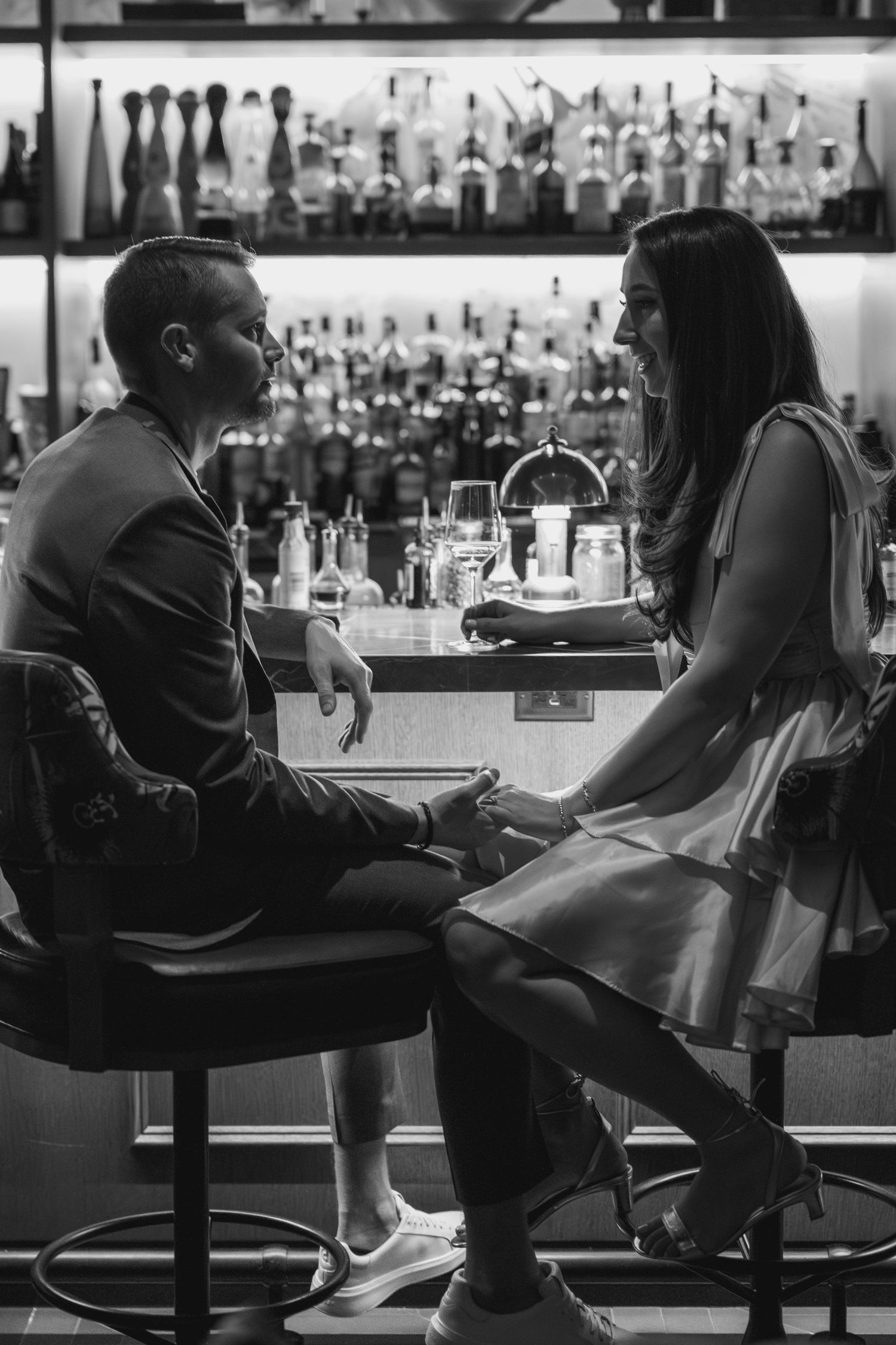 Black and white photo of people sitting at a bar counter in silhouette with glasses and bottles in the background.