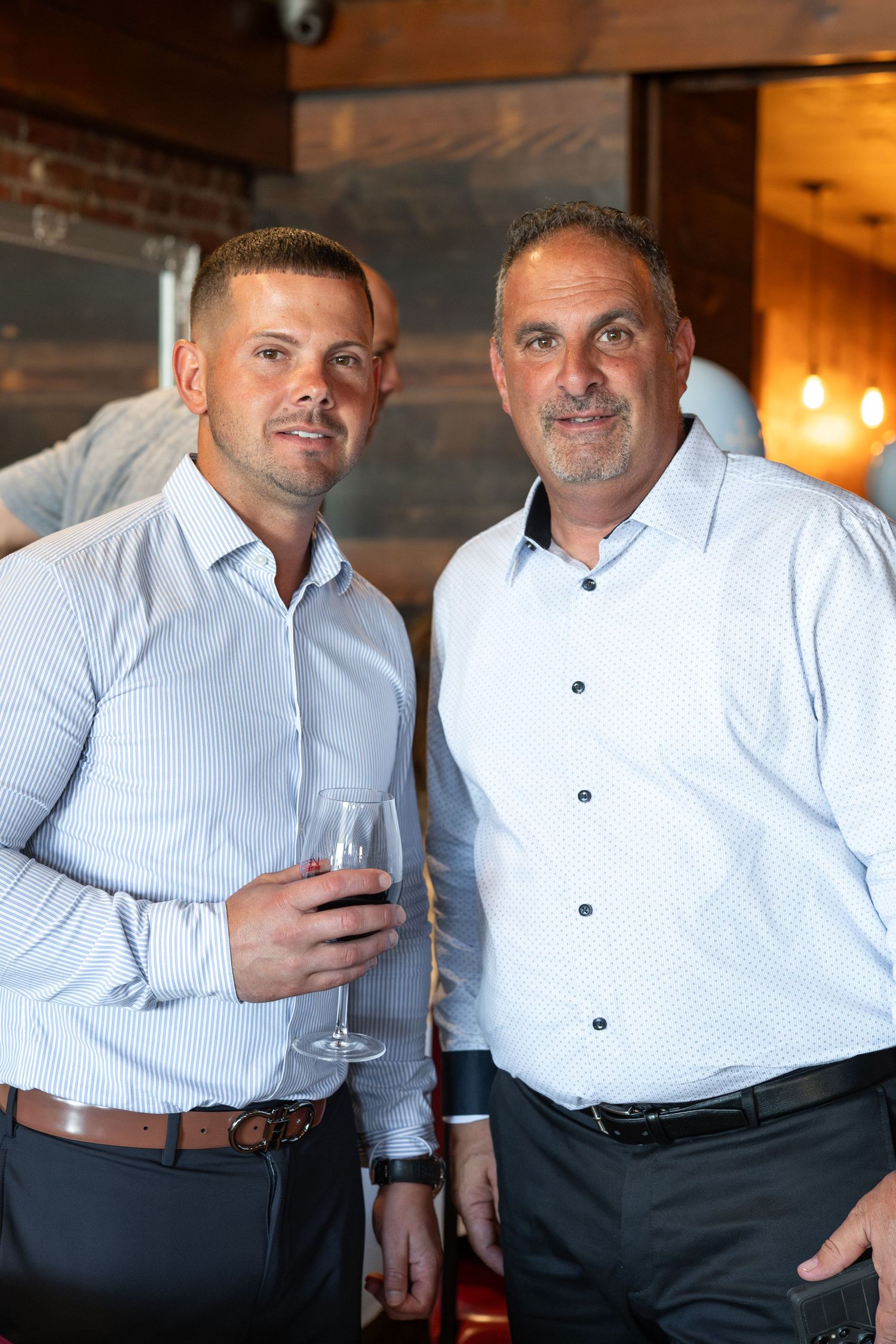Two men in formal attire enjoying drinks and conversation at an indoor venue.