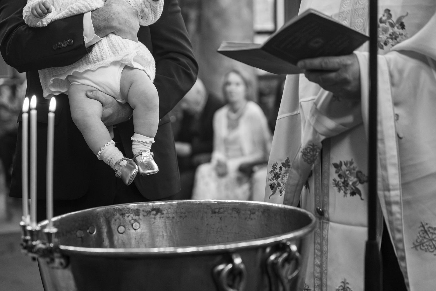 Black and white photo of a baby being held over a baptismal font during a Christian christening ceremony.