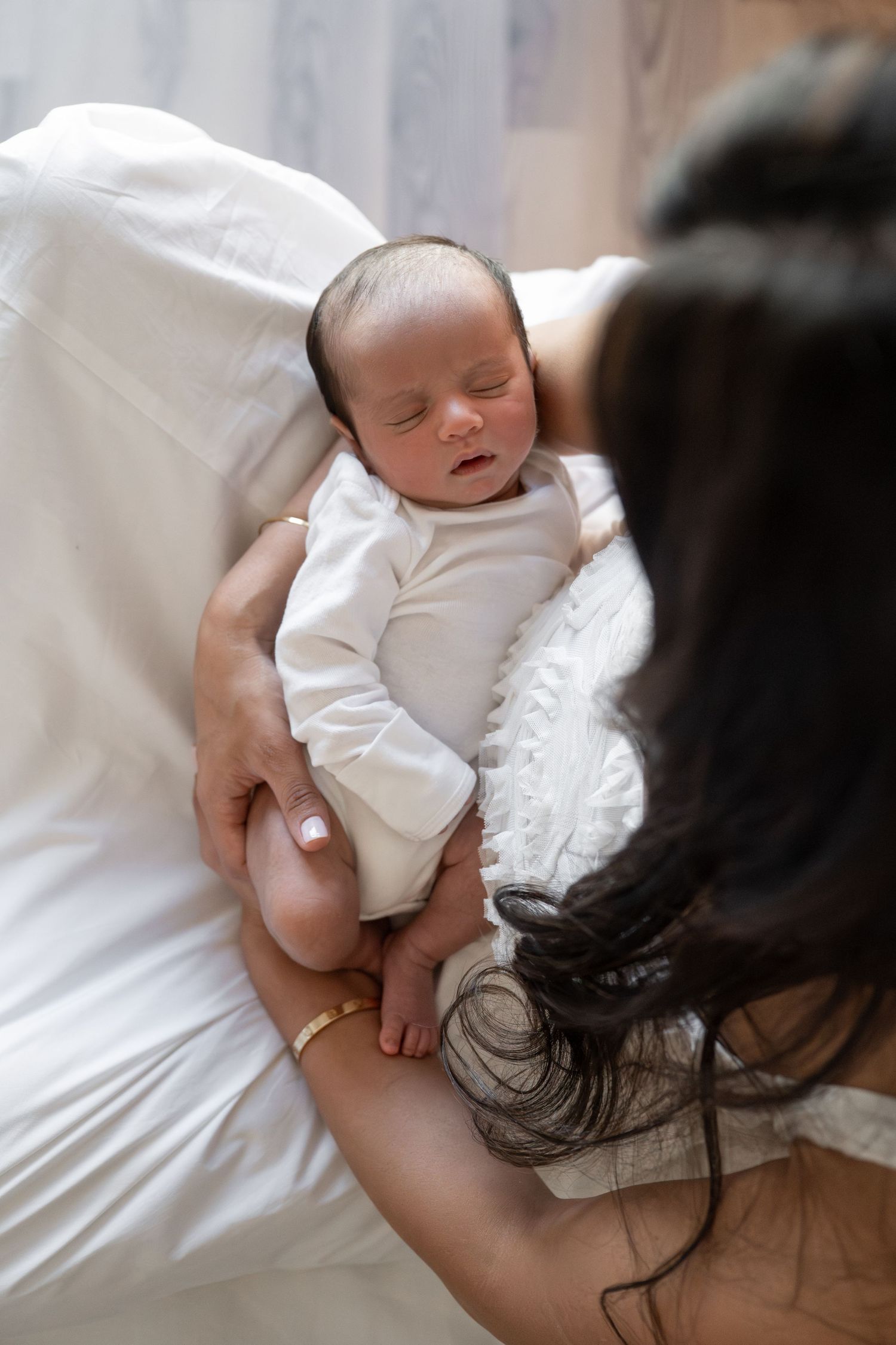 Newborn baby sleeping peacefully in white clothing on white bedding.