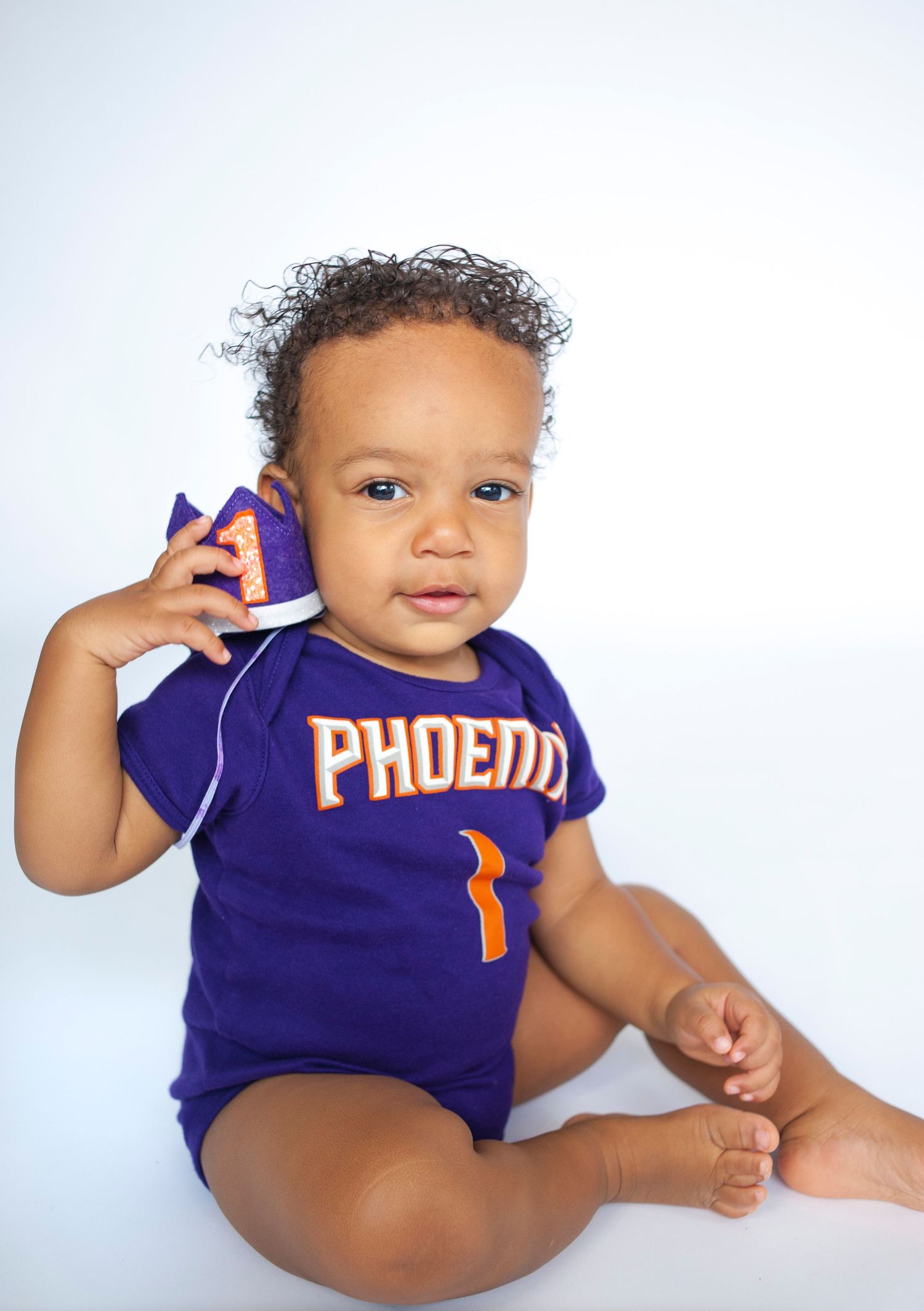 Baby wearing purple Phoenix basketball jersey sitting against white background.