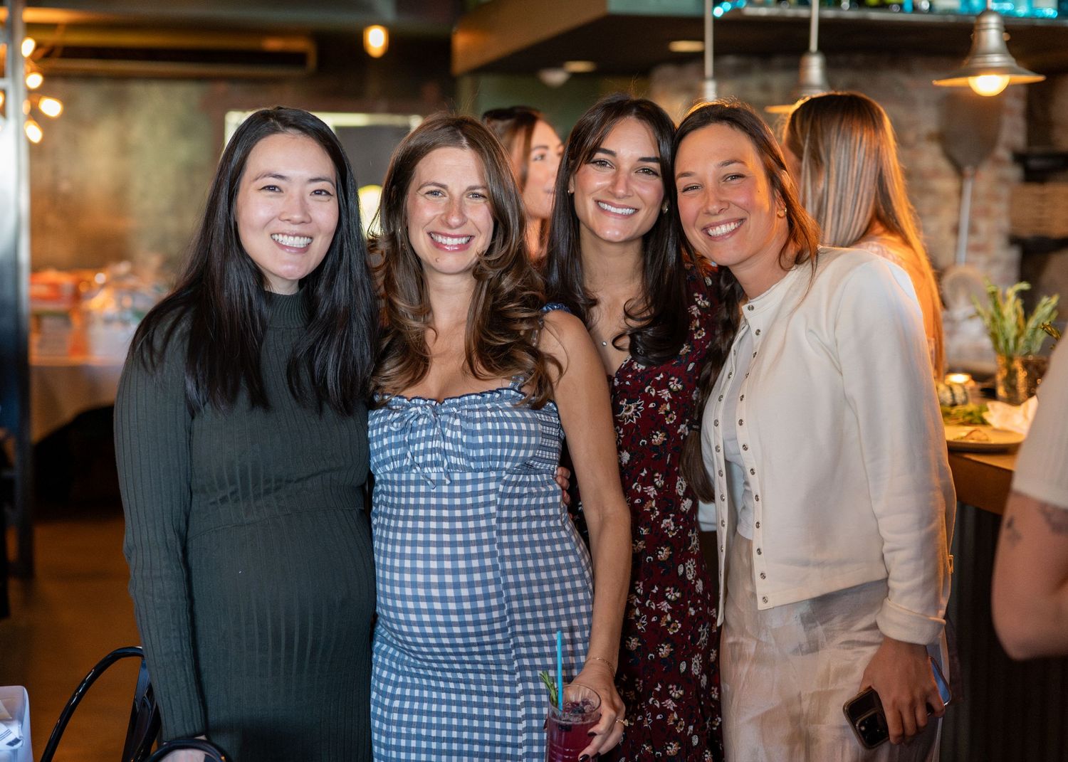 A group of friends smiling and posing together at a social gathering in a cozy indoor venue.