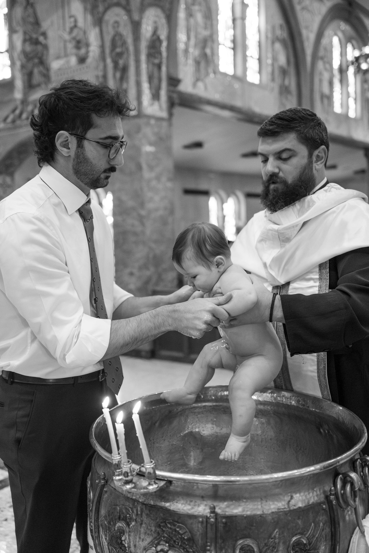 A baby being baptized in a traditional church font with clergy performing the ceremony.
