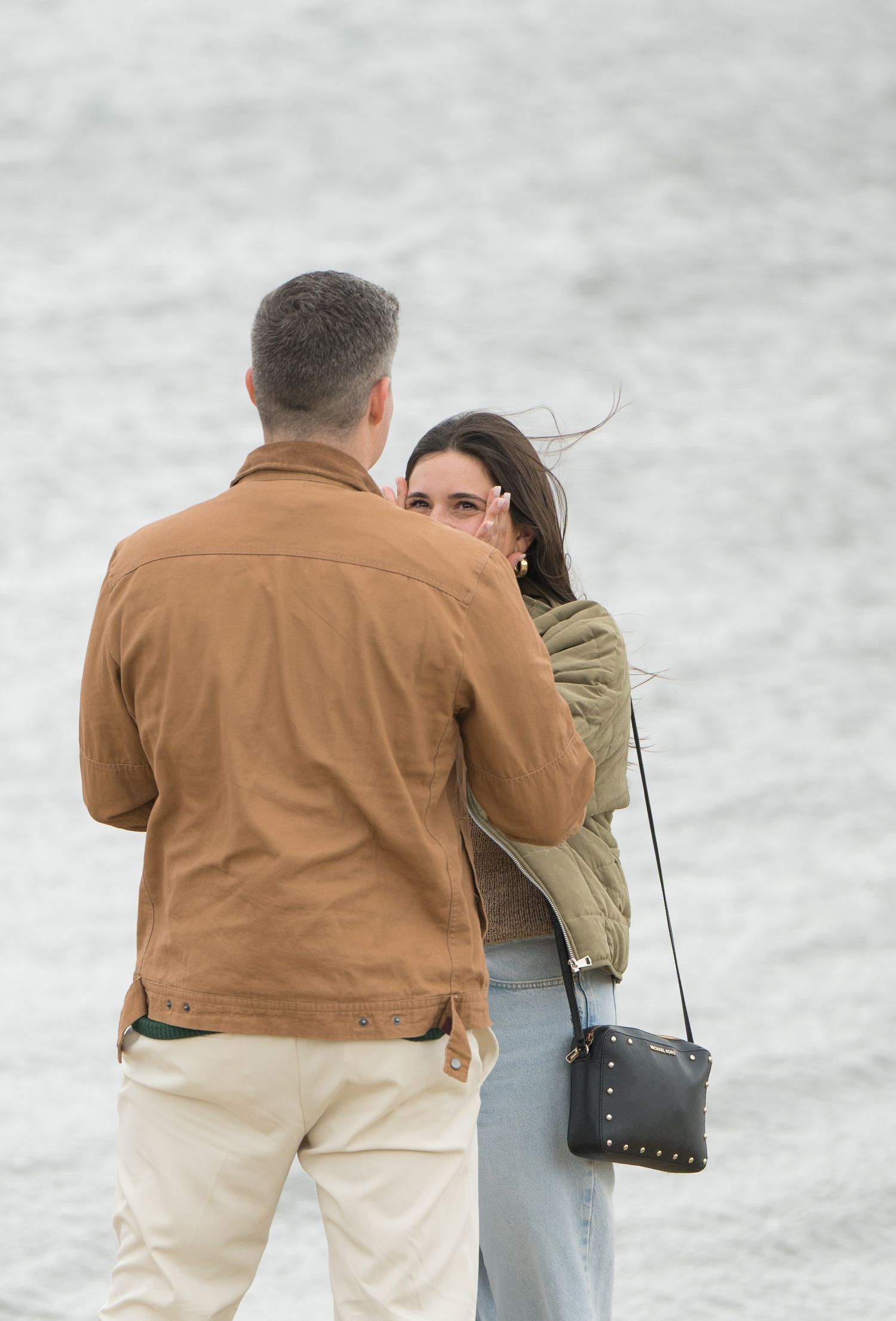 A couple shares an intimate moment on a beach wearing casual clothing in warm lighting.