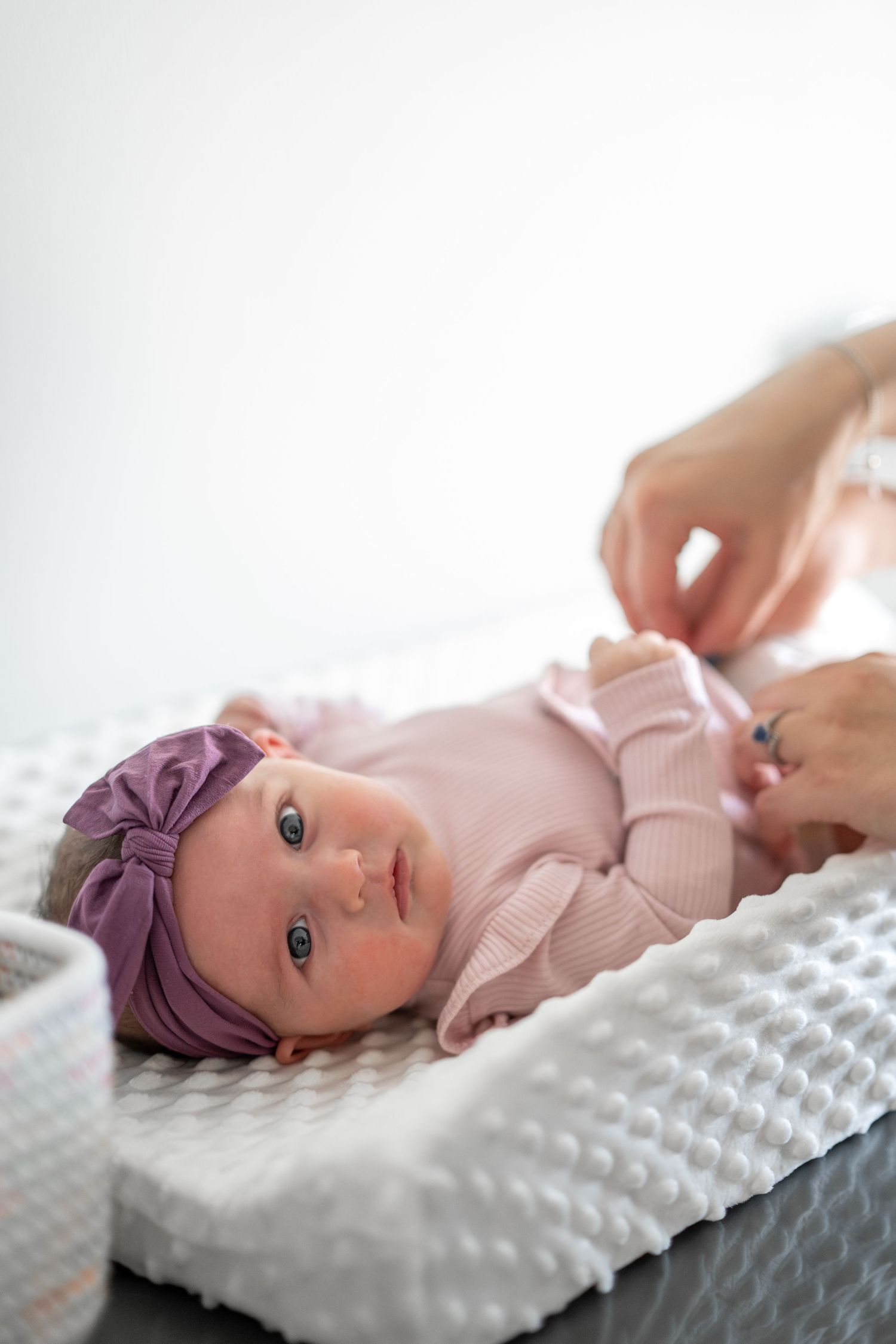 Baby wearing purple headband rests on textured white pillow in soft natural light.