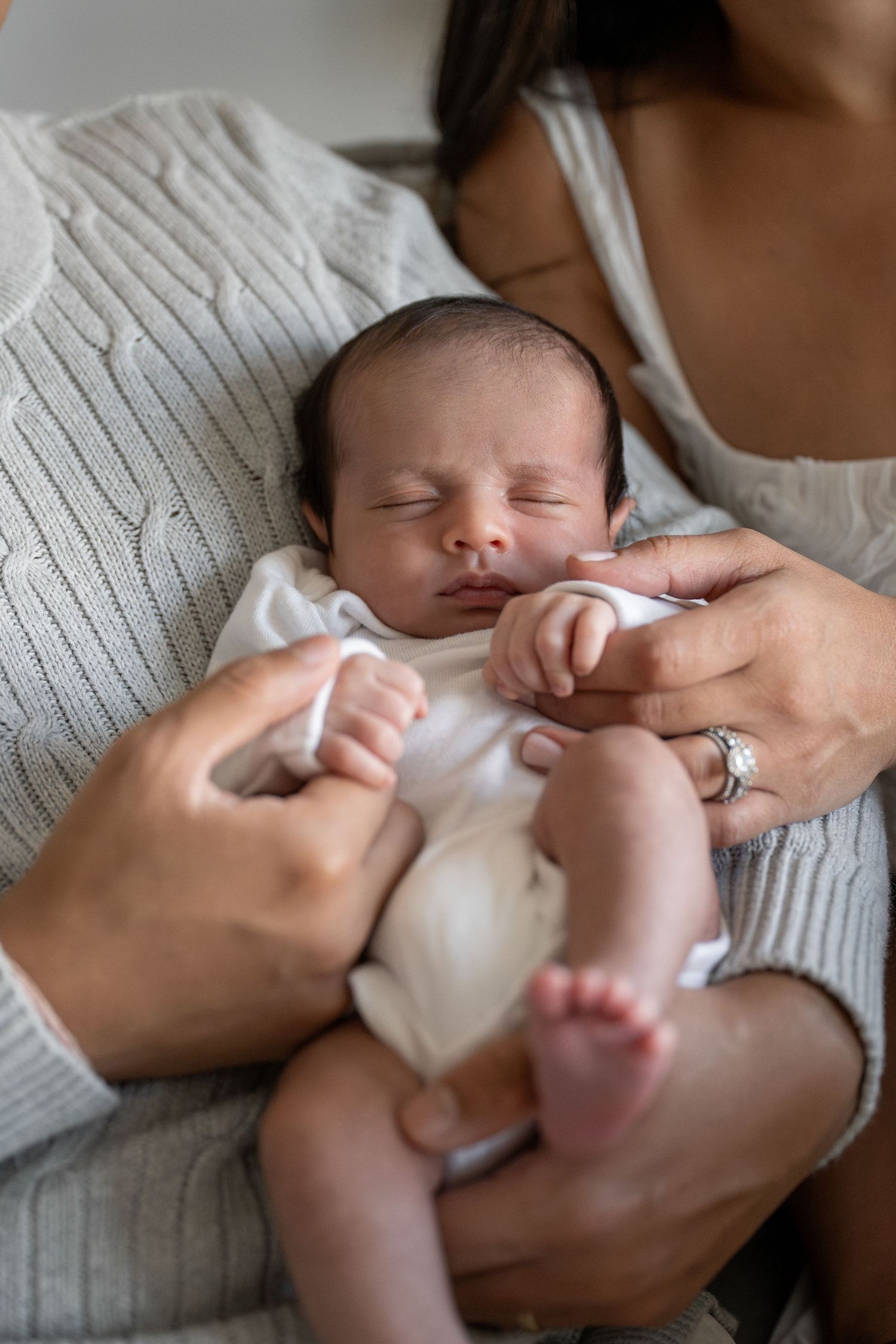 Sleeping newborn baby in white onesie held in gentle embrace.