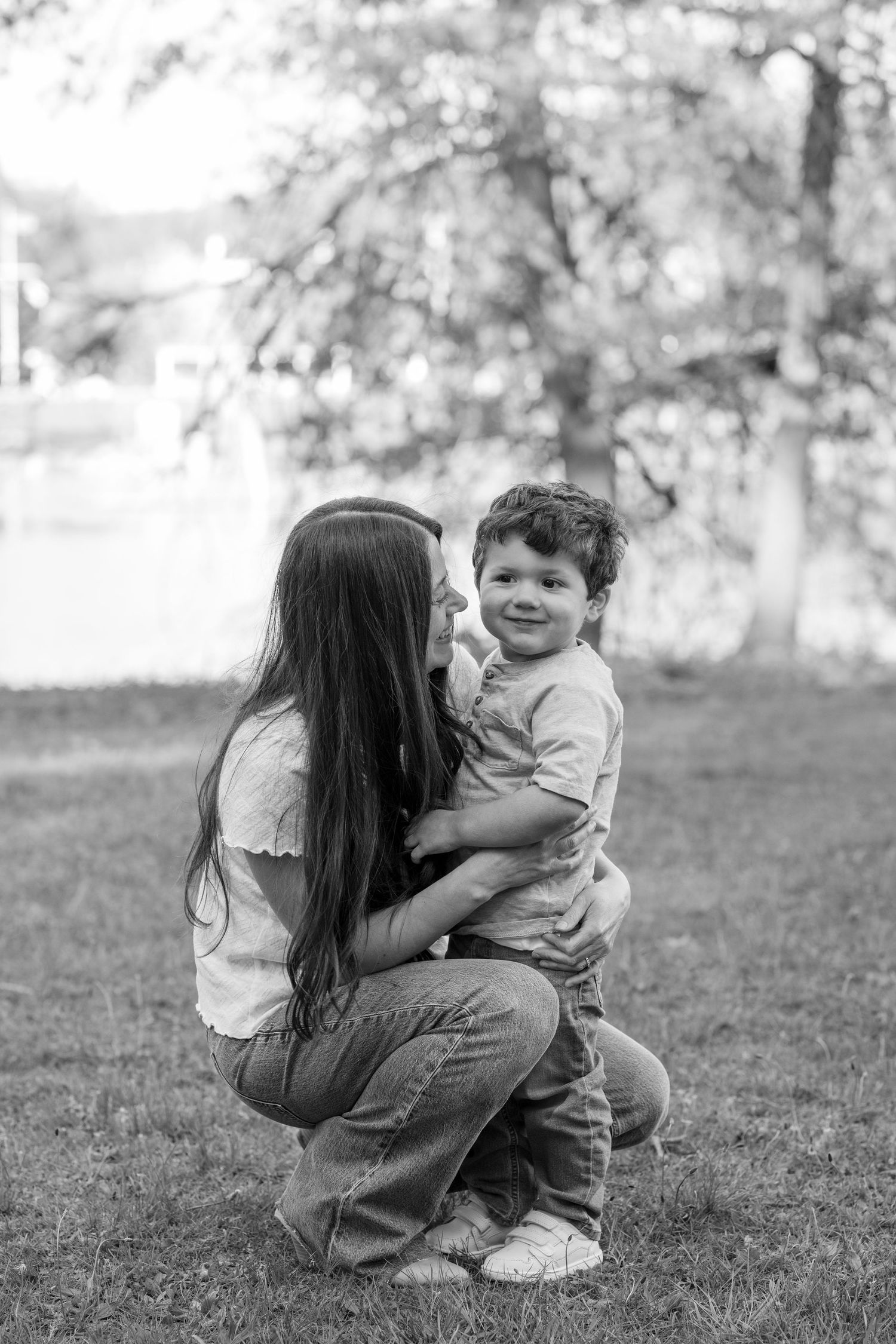 Black and white photo of a mother hugging her young son outdoors in a park setting.