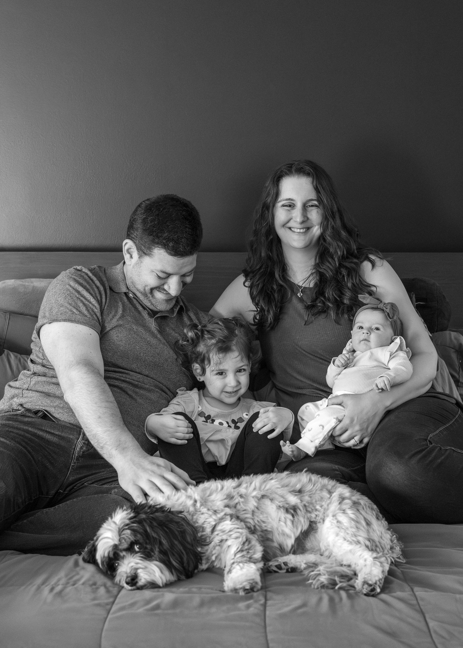 Black and white photo series showing family members relaxing on a couch with their small white dog.
