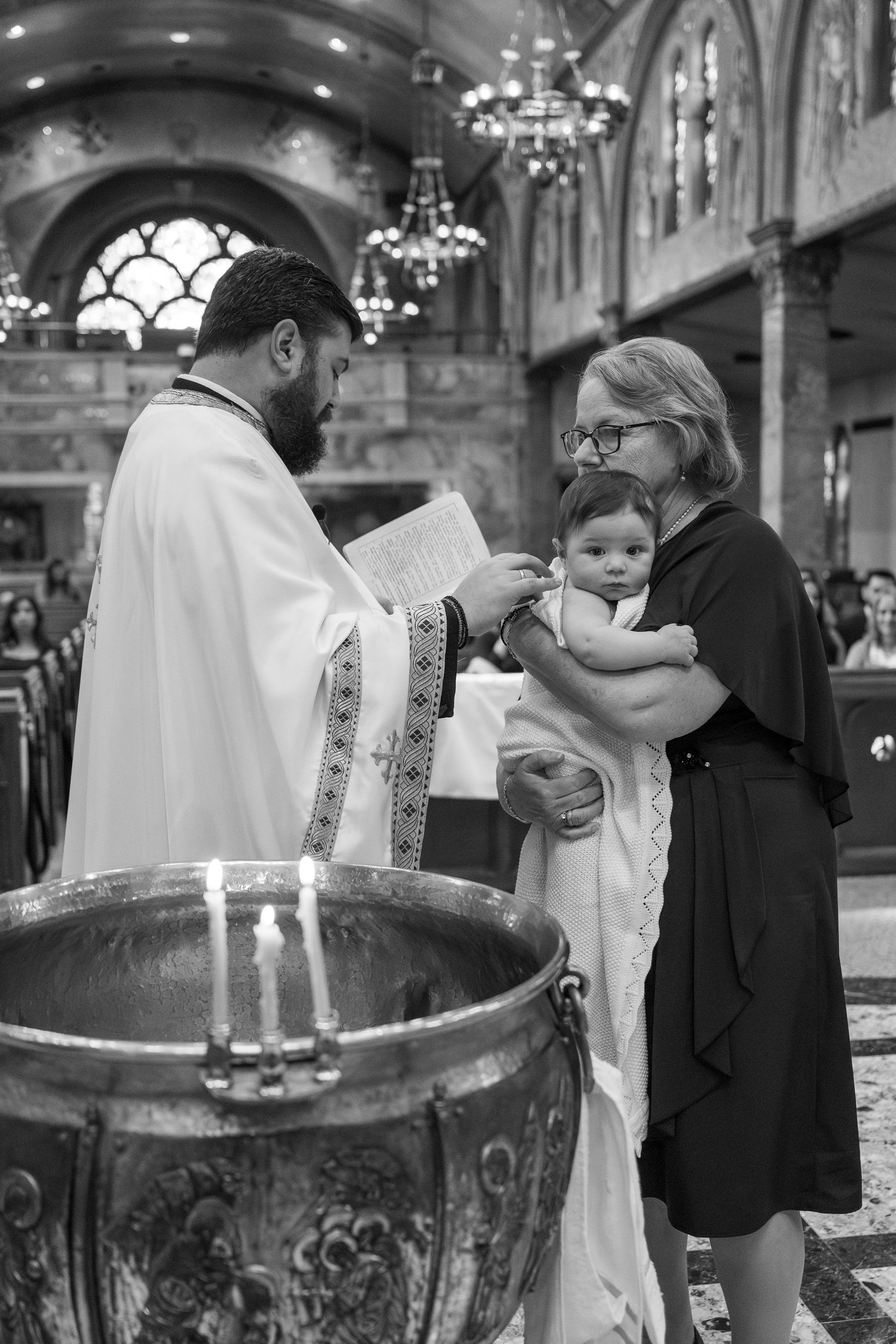 Black and white series of a baptism ceremony in a church with a priest performing the sacred ritual at a baptismal font.
