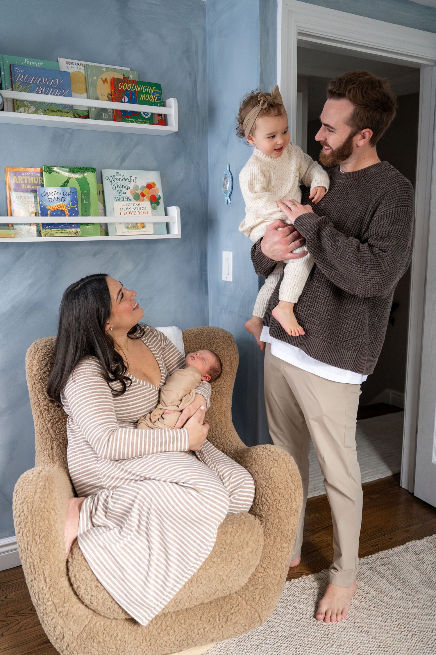 A family shares a tender moment in a nursery with bookshelves, as they care for their young children.