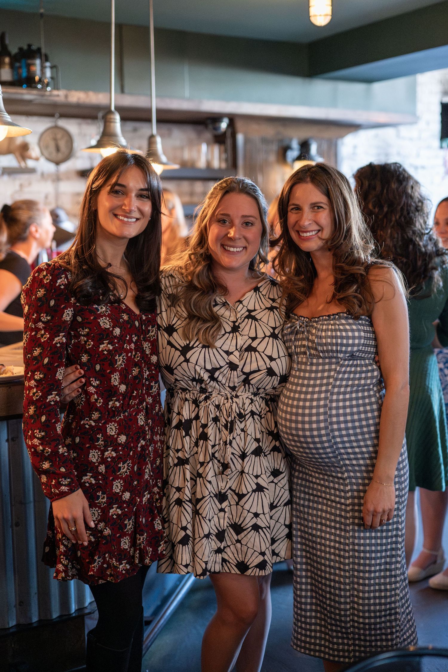 Three friends in patterned dresses posing together at a social gathering.