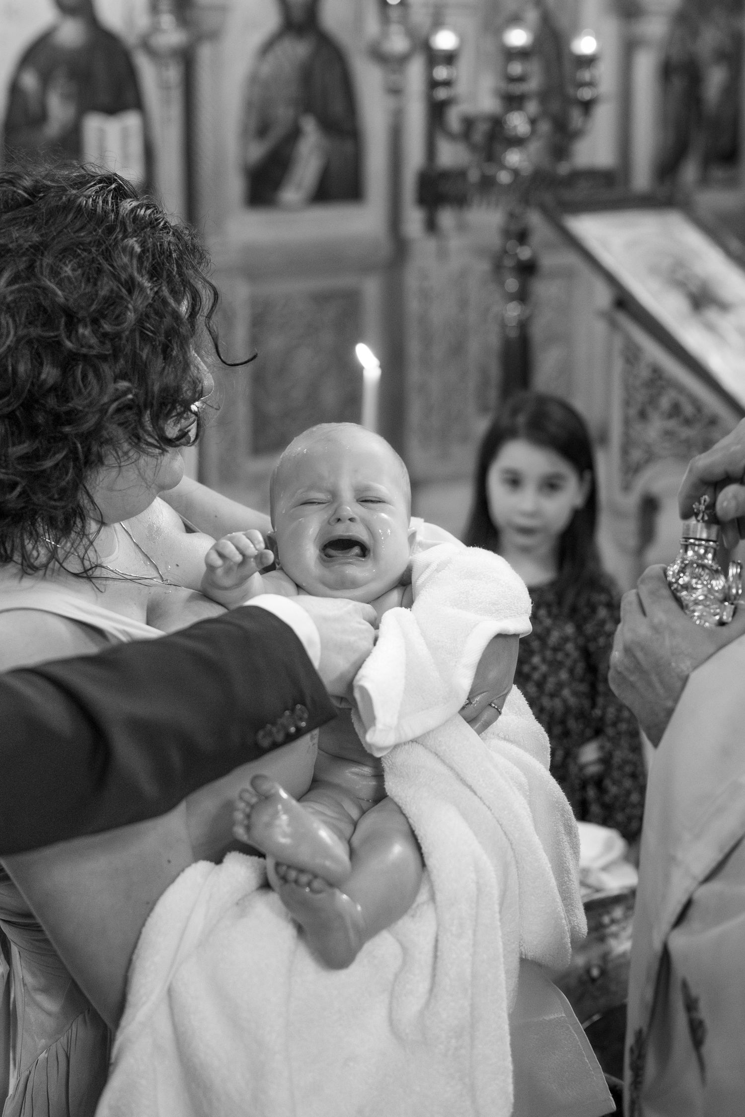 A baby in white baptismal clothing cries during a church ceremony.