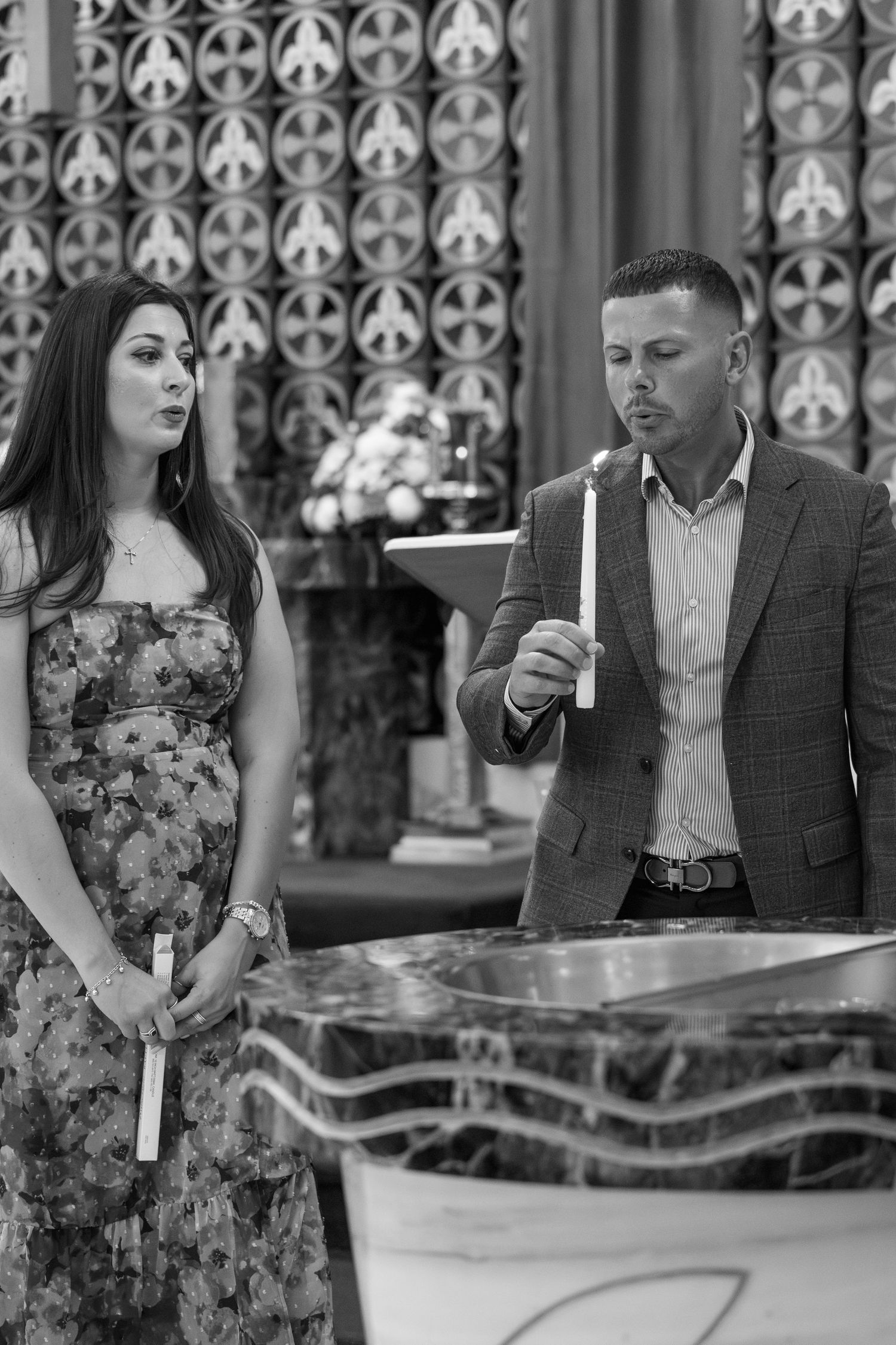 Two people holding candles during a religious ceremony in front of decorative church architecture.