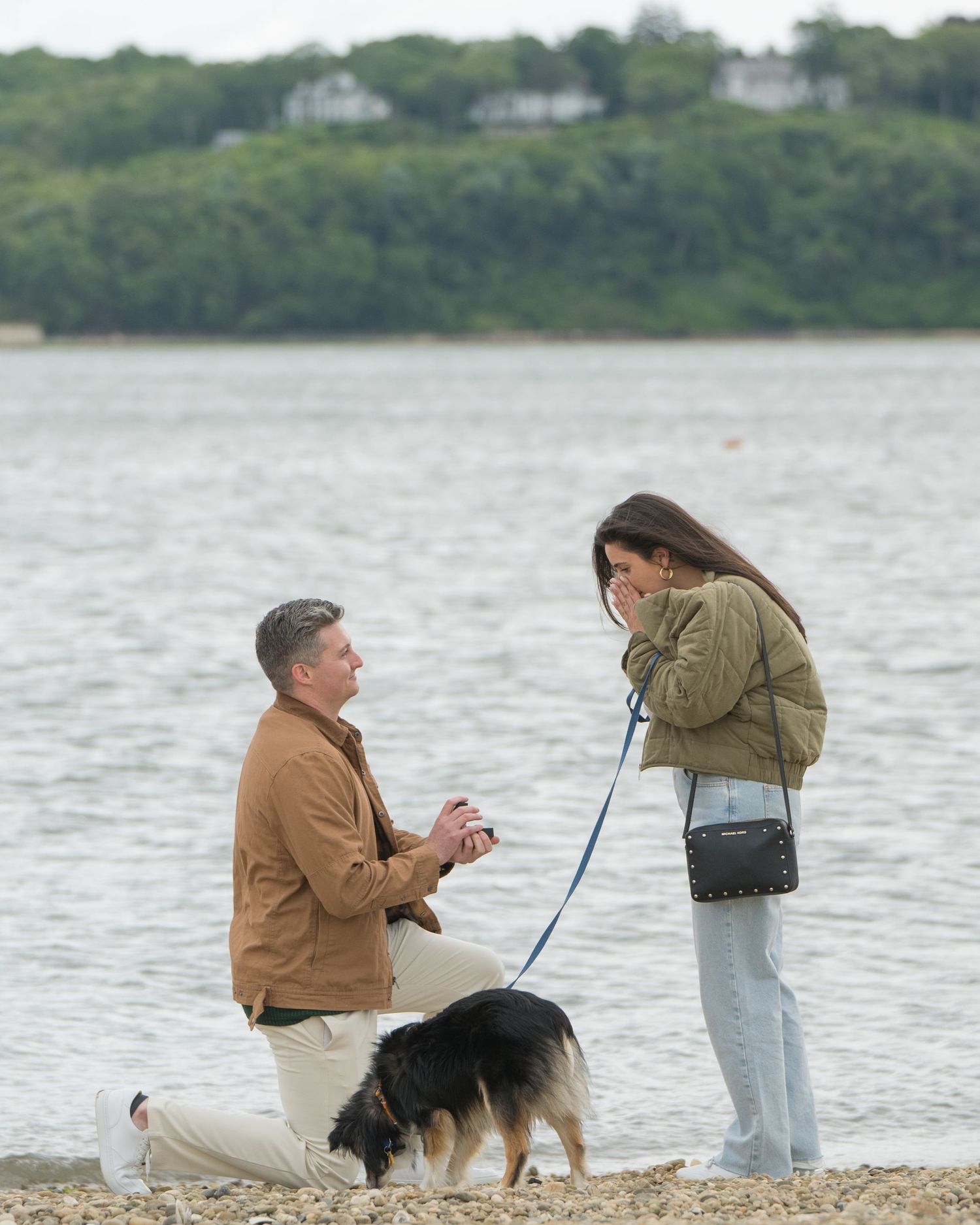 A couple with their black dog enjoy a romantic moment together on a beach by the water.
