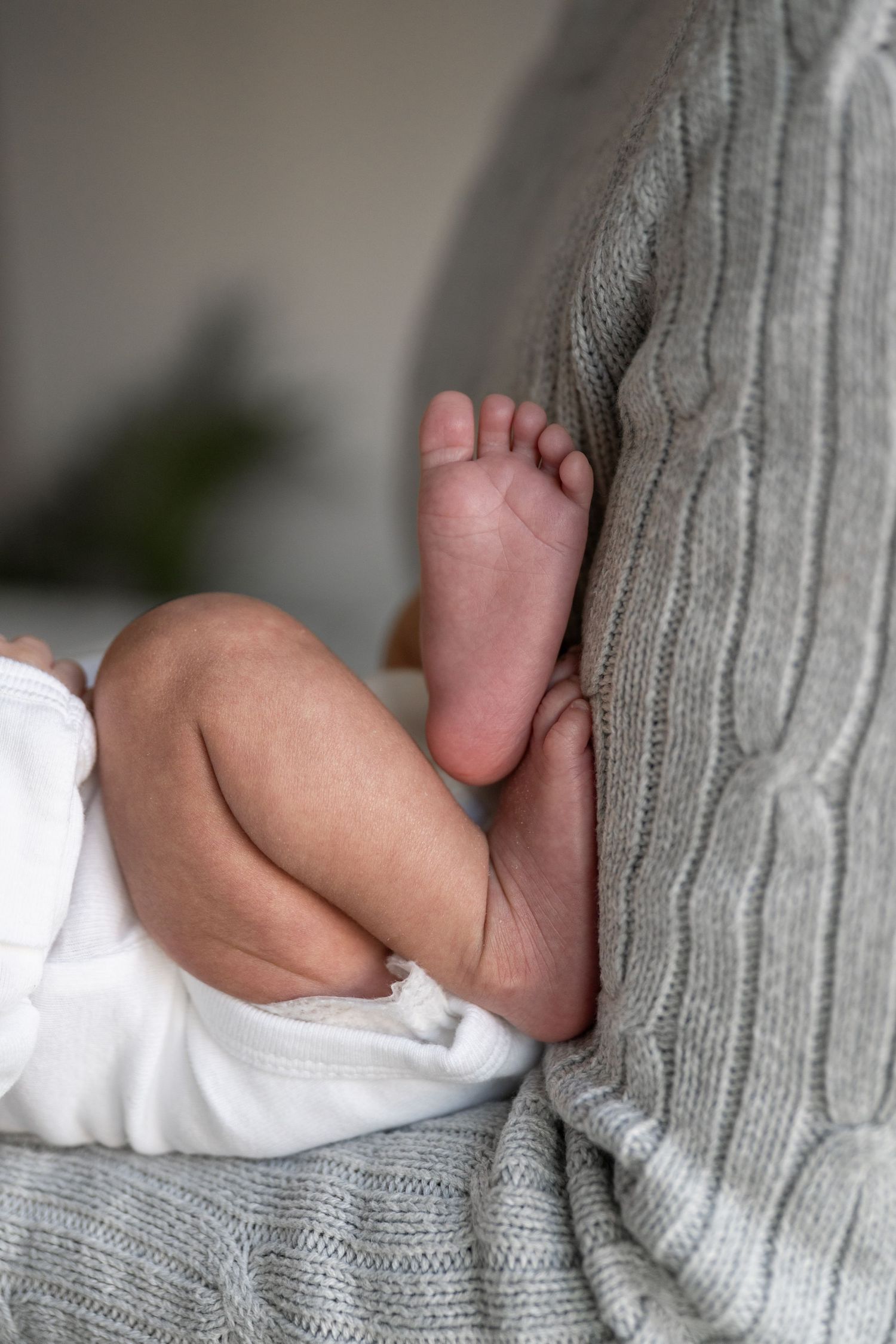 Close-up of tiny baby feet and legs resting against a gray knitted sweater.
