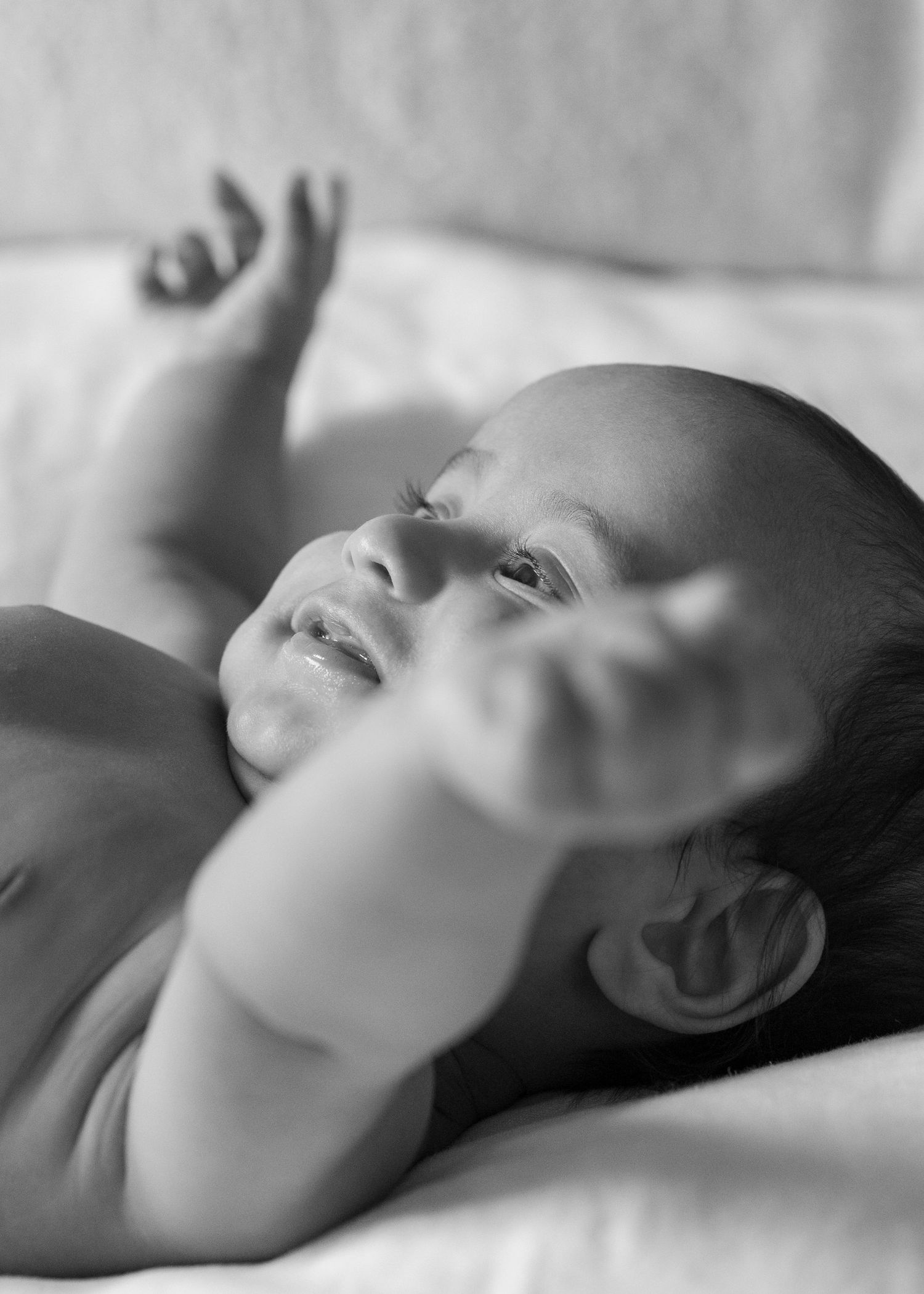 Black and white photo of newborn baby lying on back reaching arm upward with soft focus.