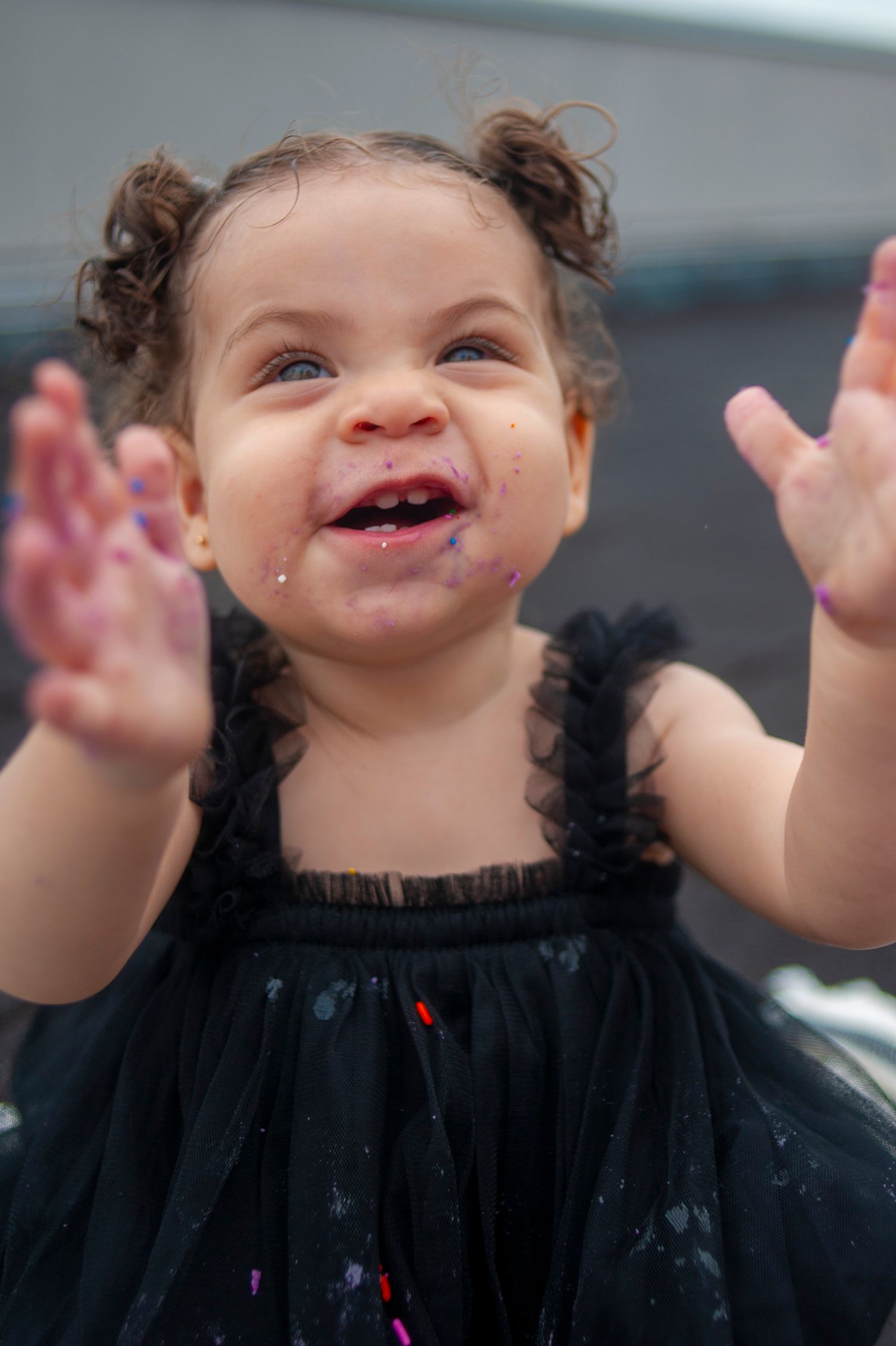 Joyful child in black dress raising messy hands with a big smile.