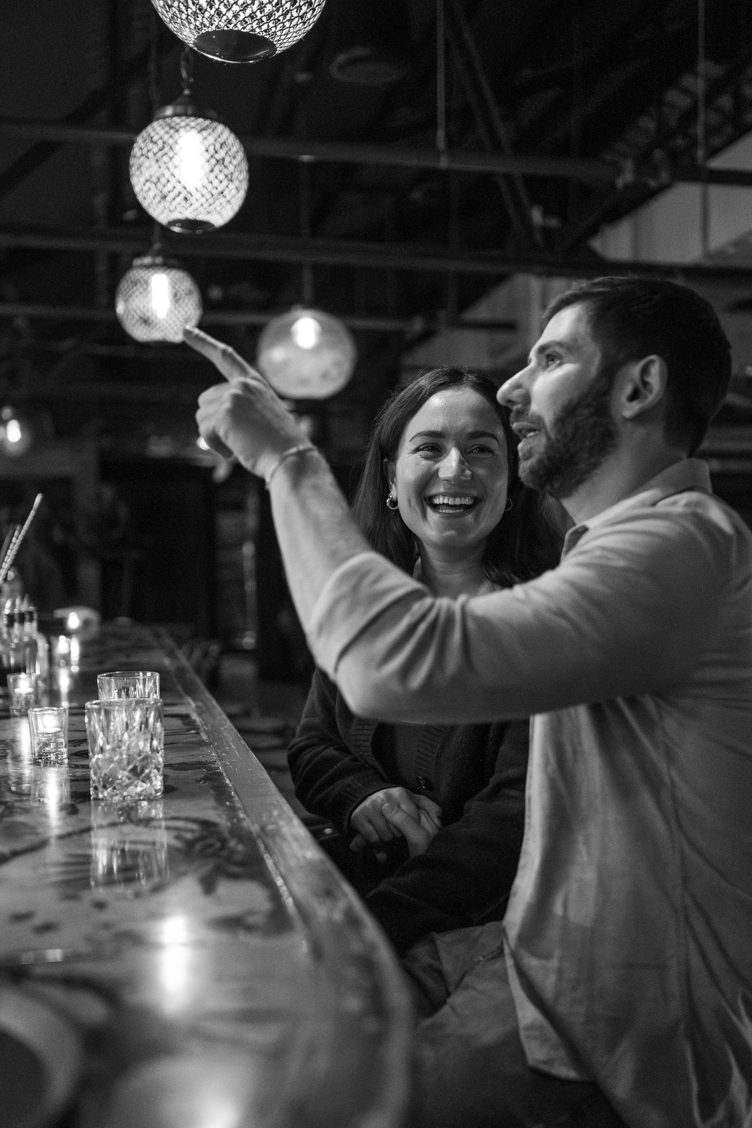 People socializing and laughing together at a bar with decorative hanging lights in the background.