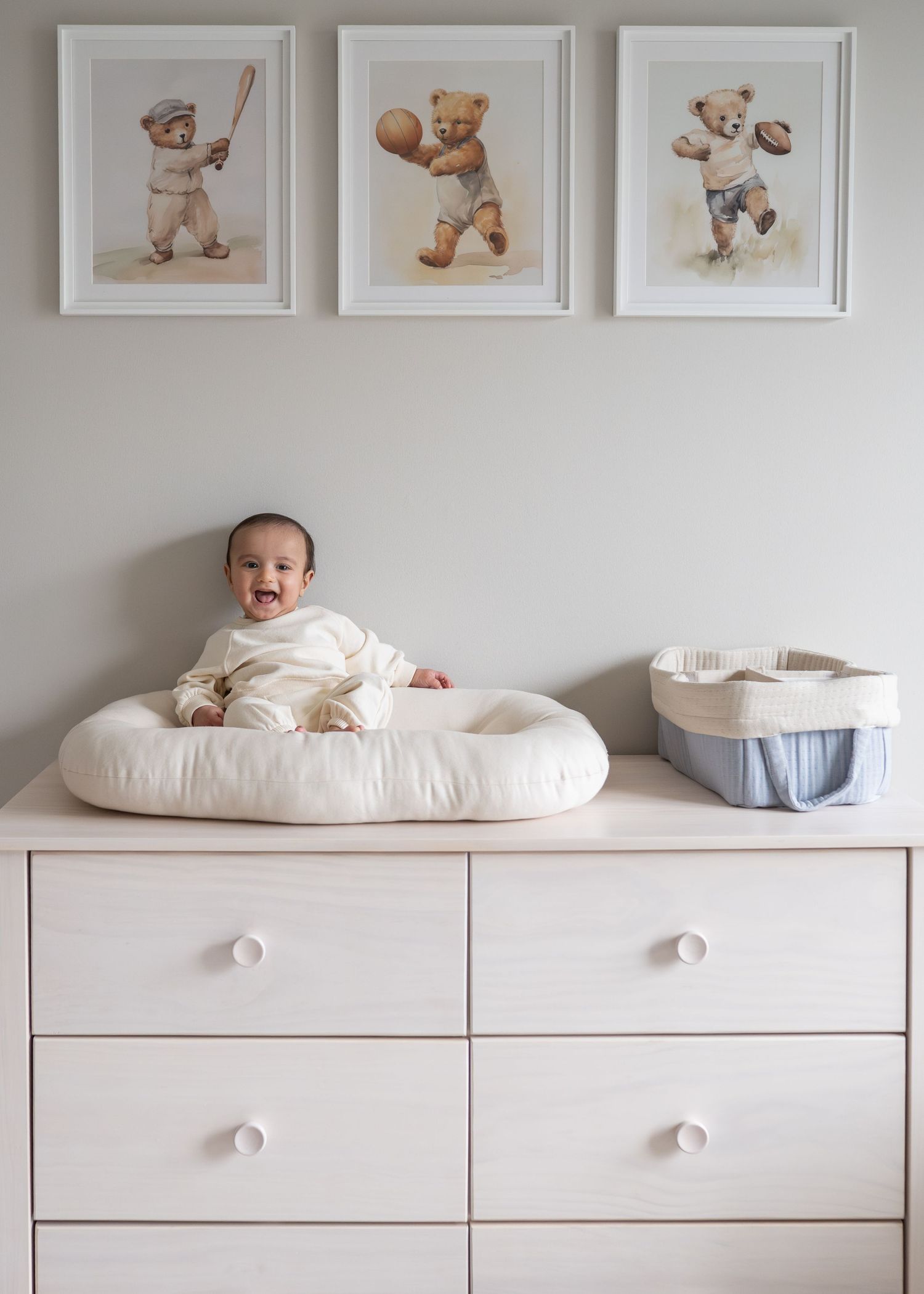 White nursery wall with framed teddy bear artwork and matching white dresser displaying plush toys and baby essentials.