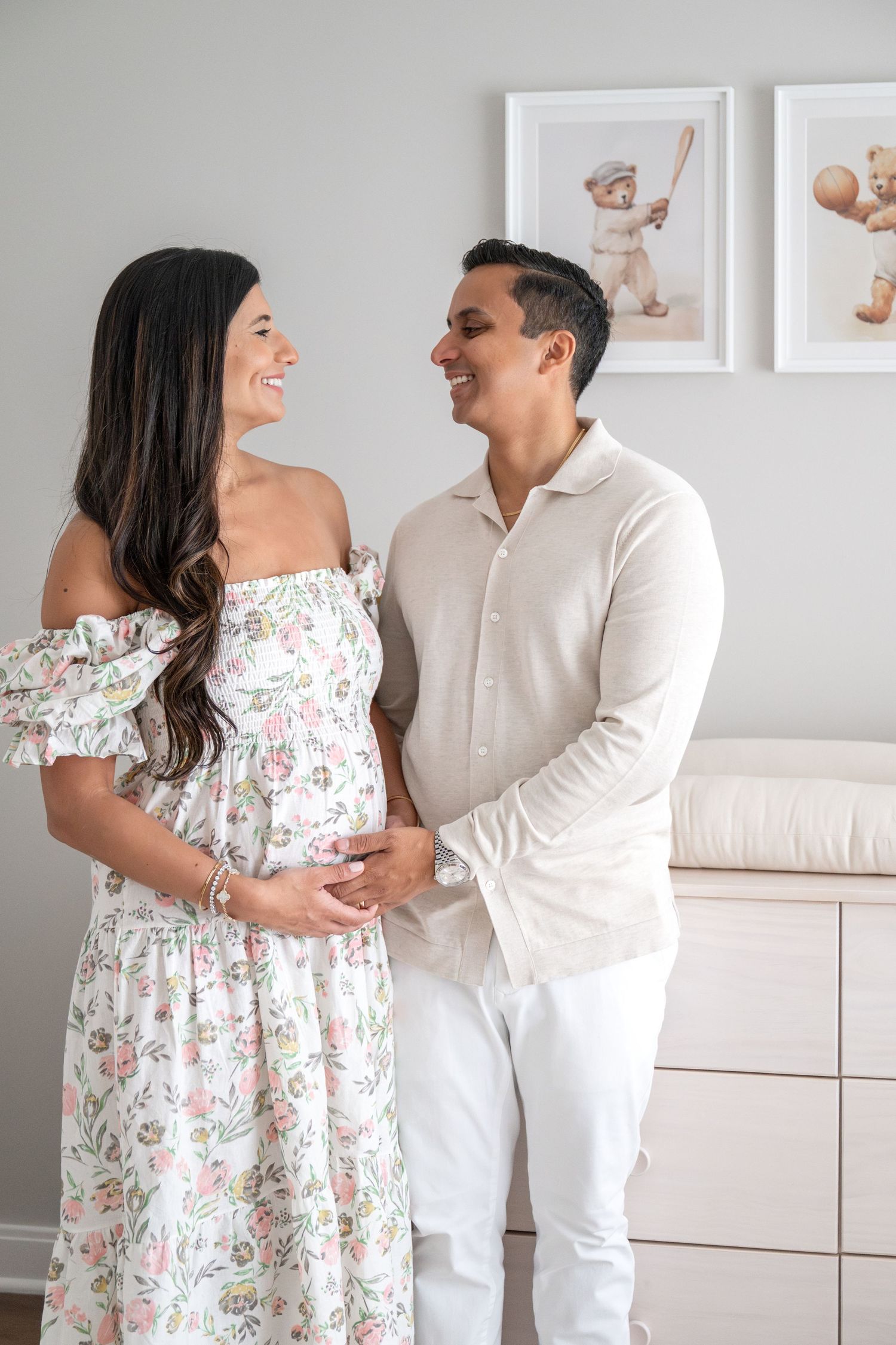 Couple sharing joyful moments in nursery with white furniture and baby photos on wall.