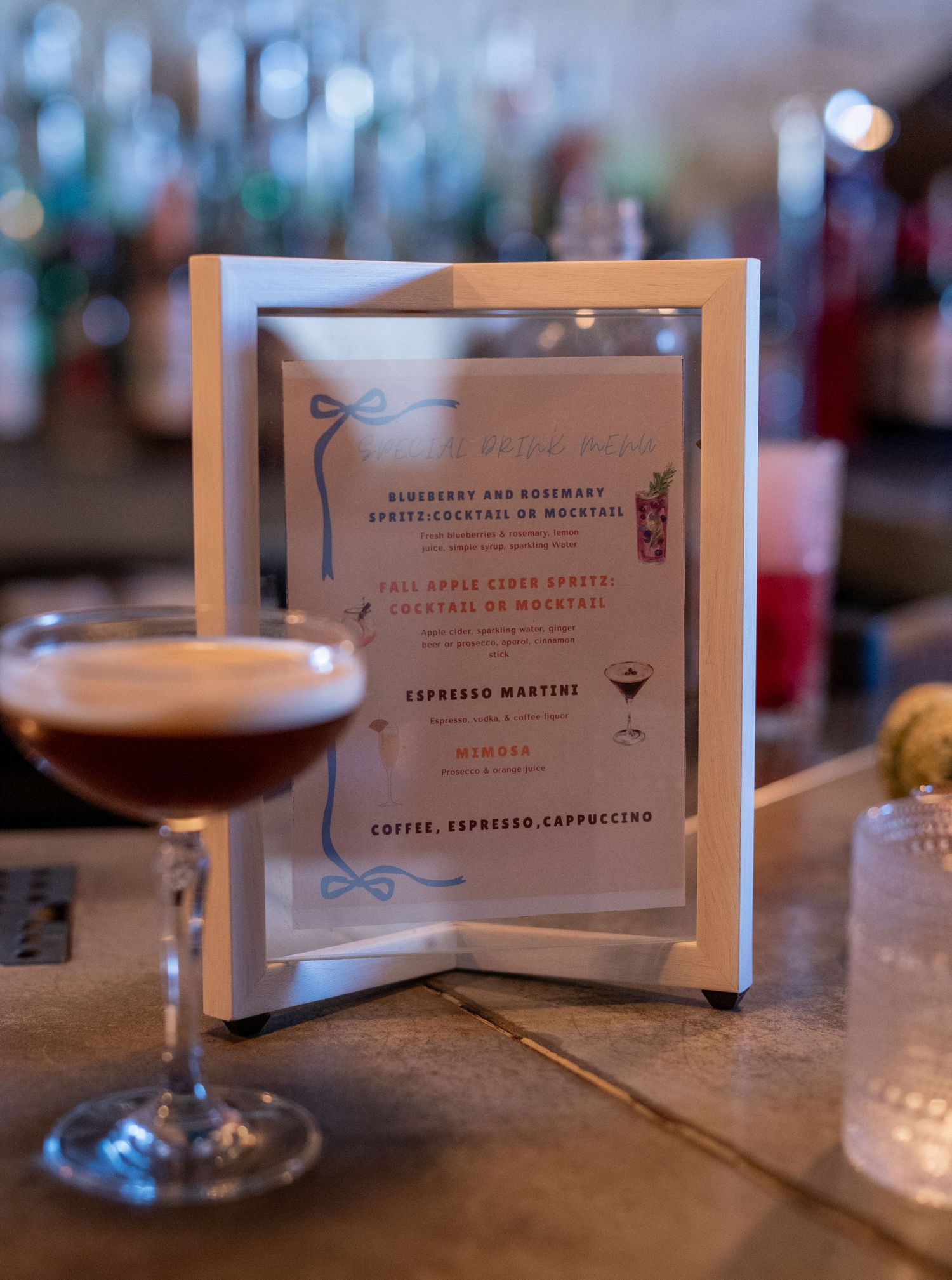 Elegant cocktail menu cards and drinks displayed on a dimly lit bar counter with soft bokeh lighting in the background.