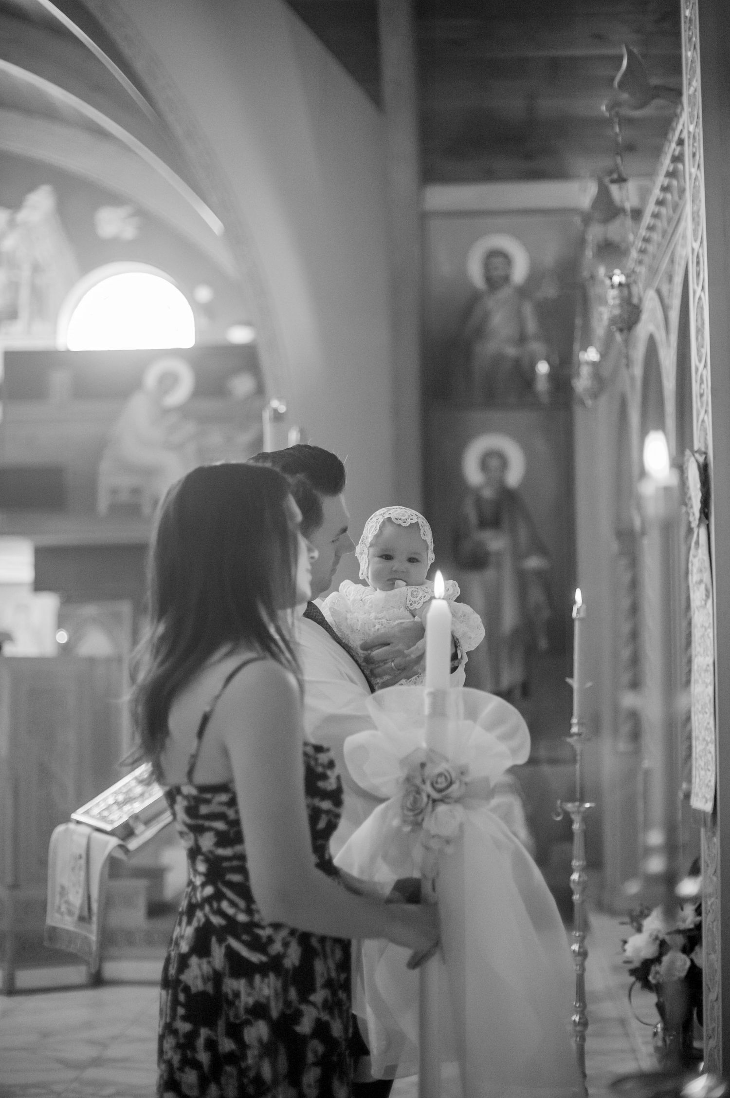 A baby in a white dress is being carried through a hallway with reflective surfaces.